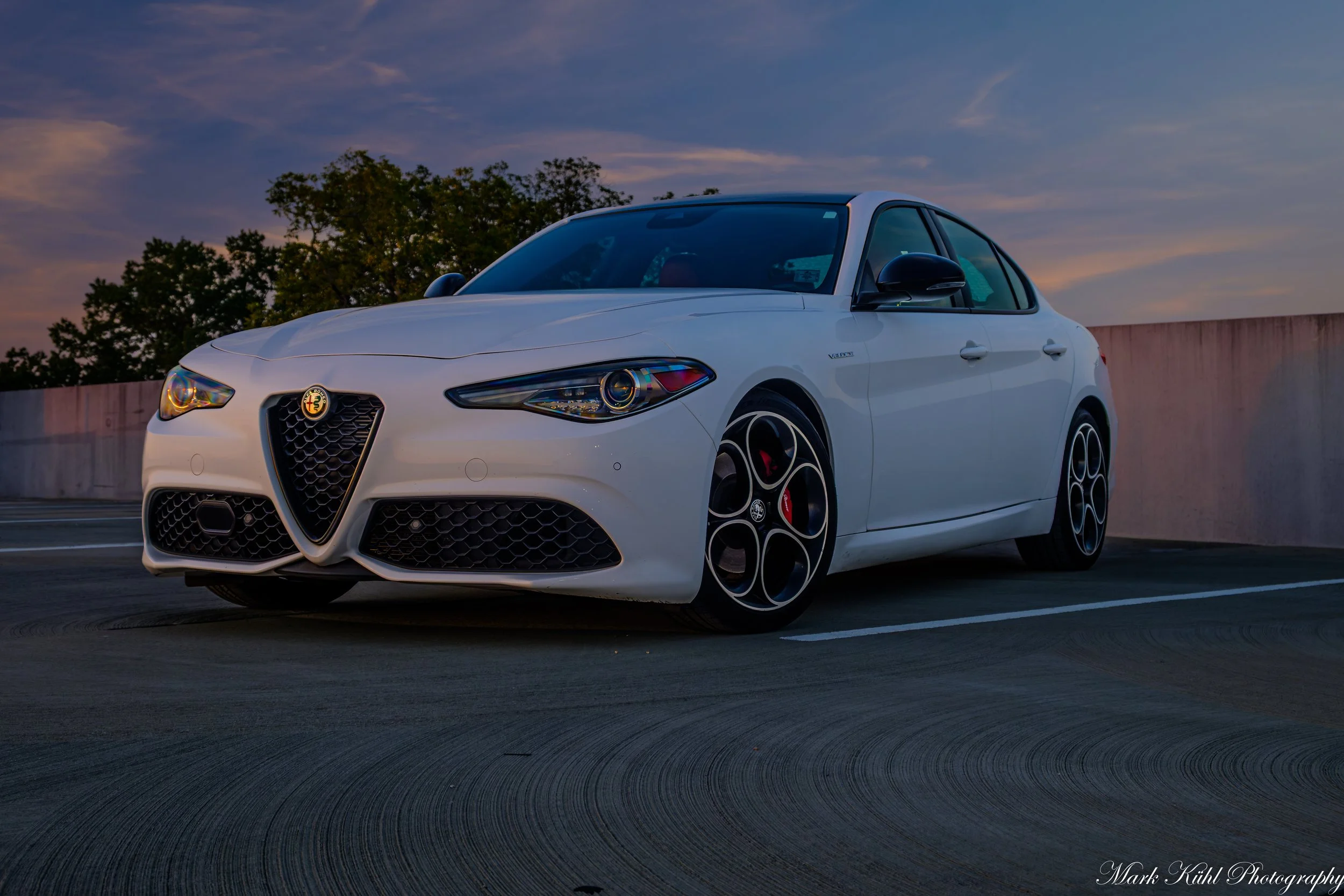 A white Alfa Romeo sedan parked outdoors during sunset photo shoot
