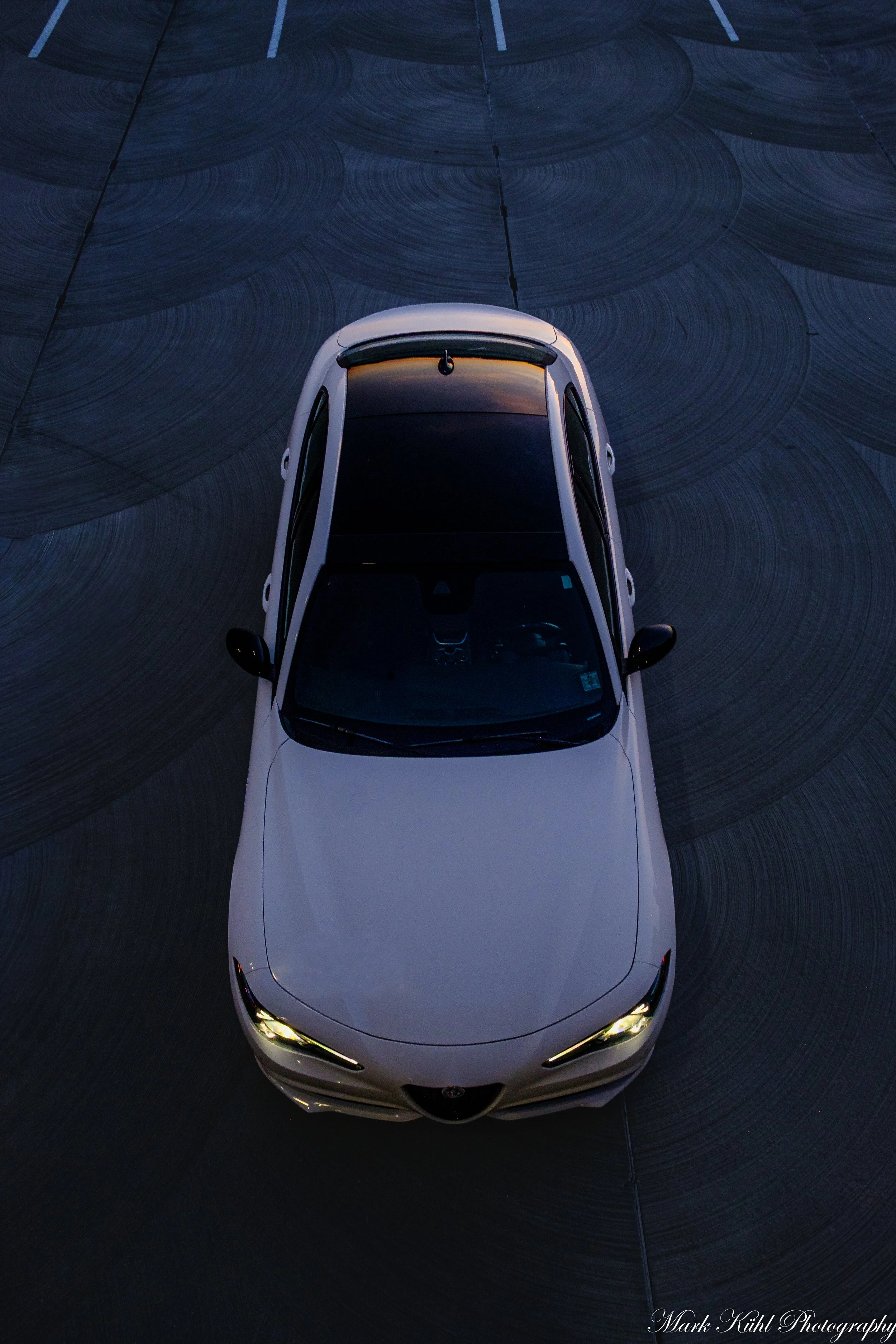 An aerial view of a white car with its headlights on, taken at dusk photo shoot.