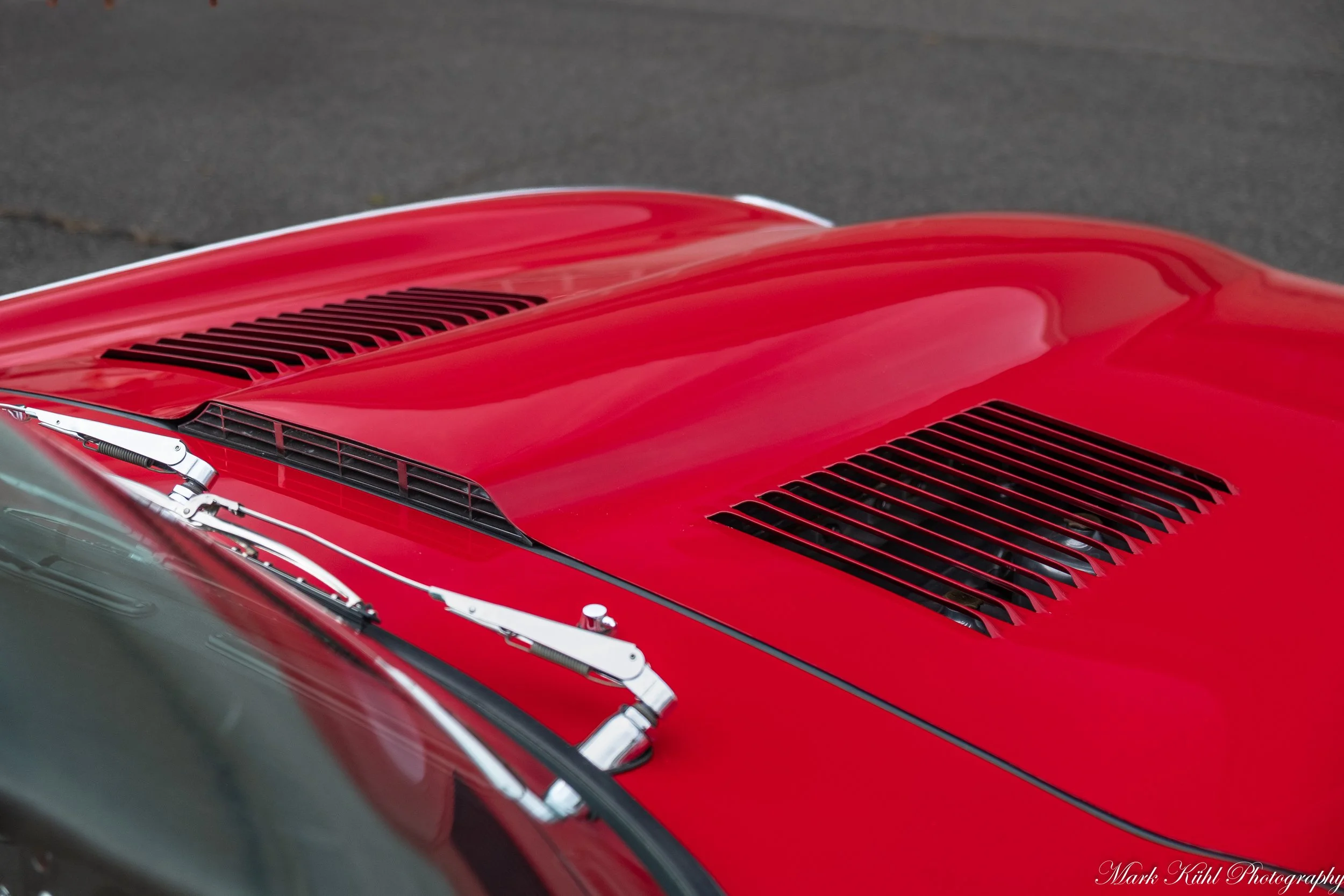 Close-up of the hood of a red classic car with vents and chrome details.