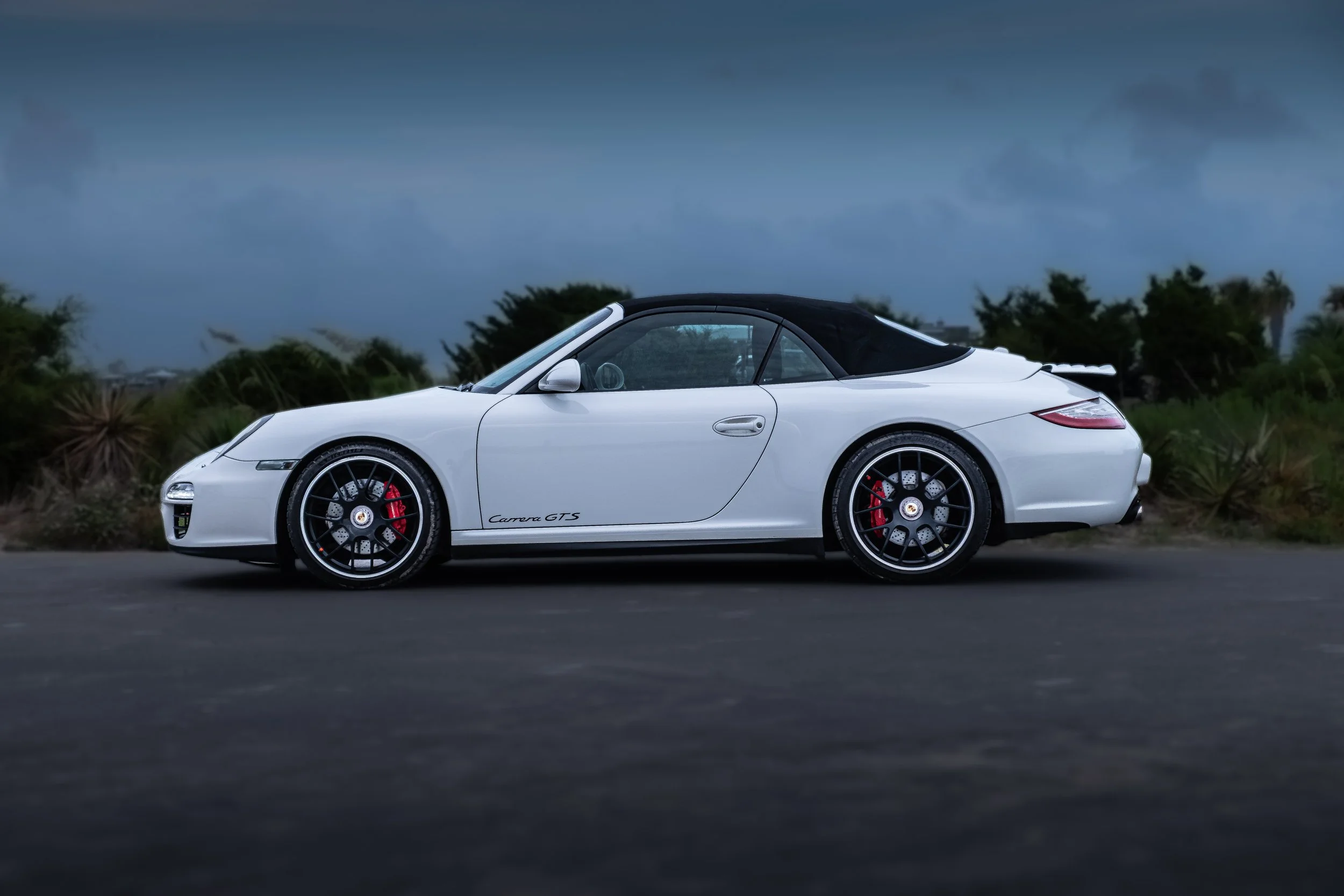 A white Porsche Carrera GTS convertible with black soft top 