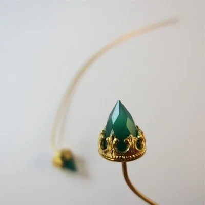 Close-up of a decorative gold and green jewellery with a pointed green gemstone