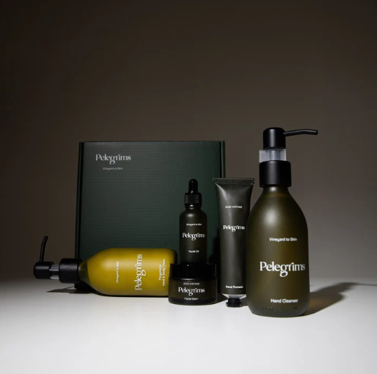 Arrangement of skincare products including a box, bottles, tubes, and jars with the brand name 'Pelegrim' on dark green and black packaging.