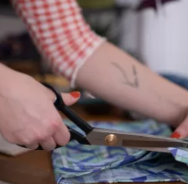Person cutting a colorful fabric with large scissors on a table.