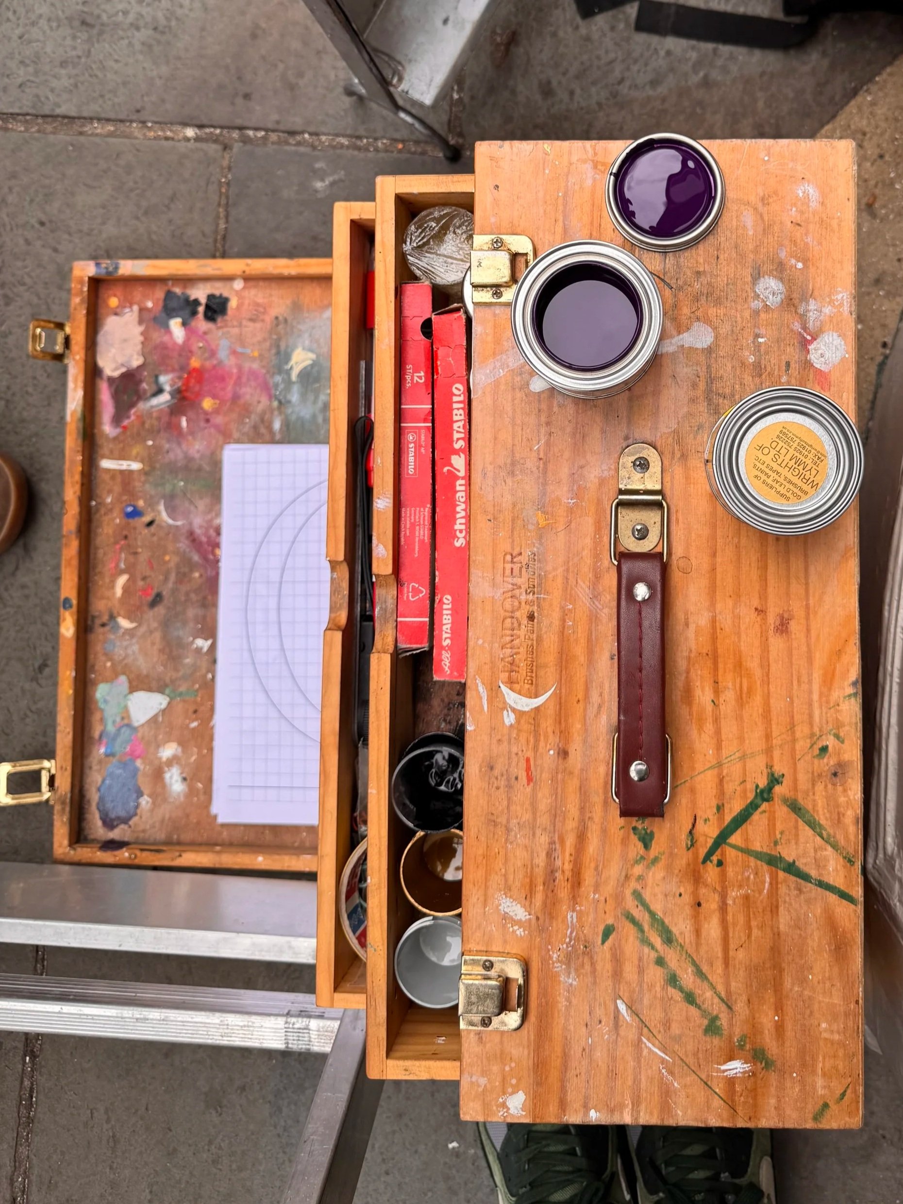 A wooden signwriters palette with open paint tins and brushes