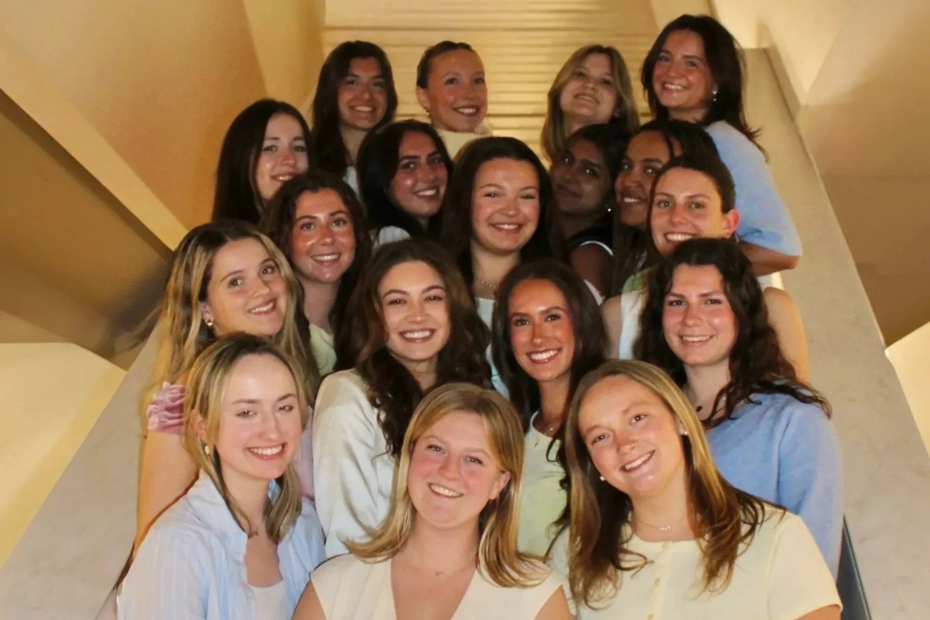 A large group of women smiling and posing for a photo on a staircase inside a building.