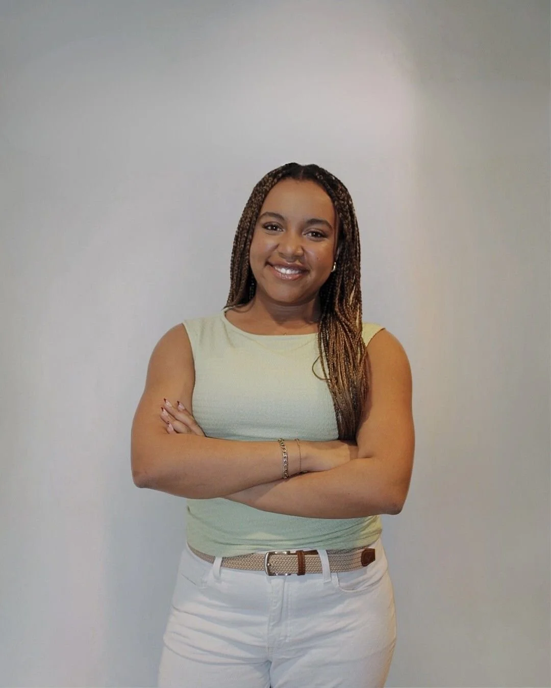 A woman standing against a plain wall, smiling, with her arms crossed.