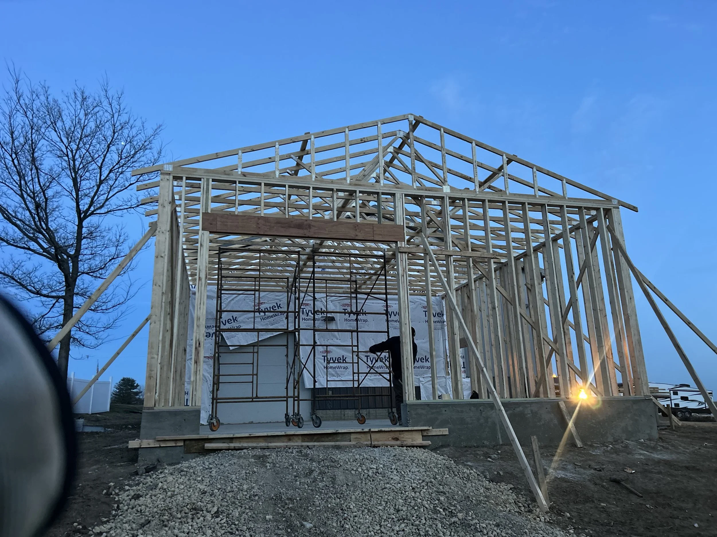 Wooden house frame under construction with clear blue sky and leafless tree in the background.