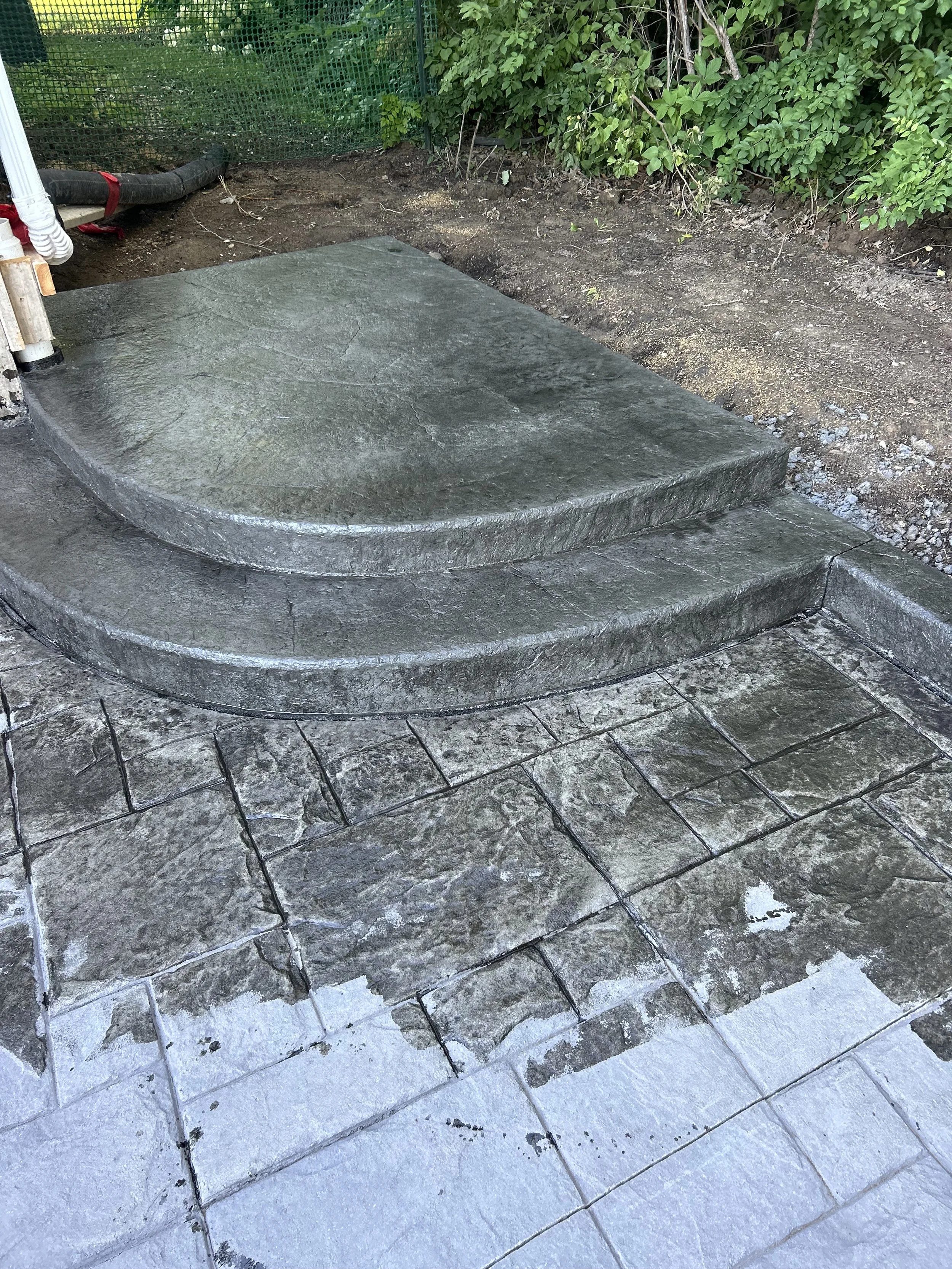 A newly installed curved concrete steps onto a patio. Completed with a stamp and two-tone finish. 