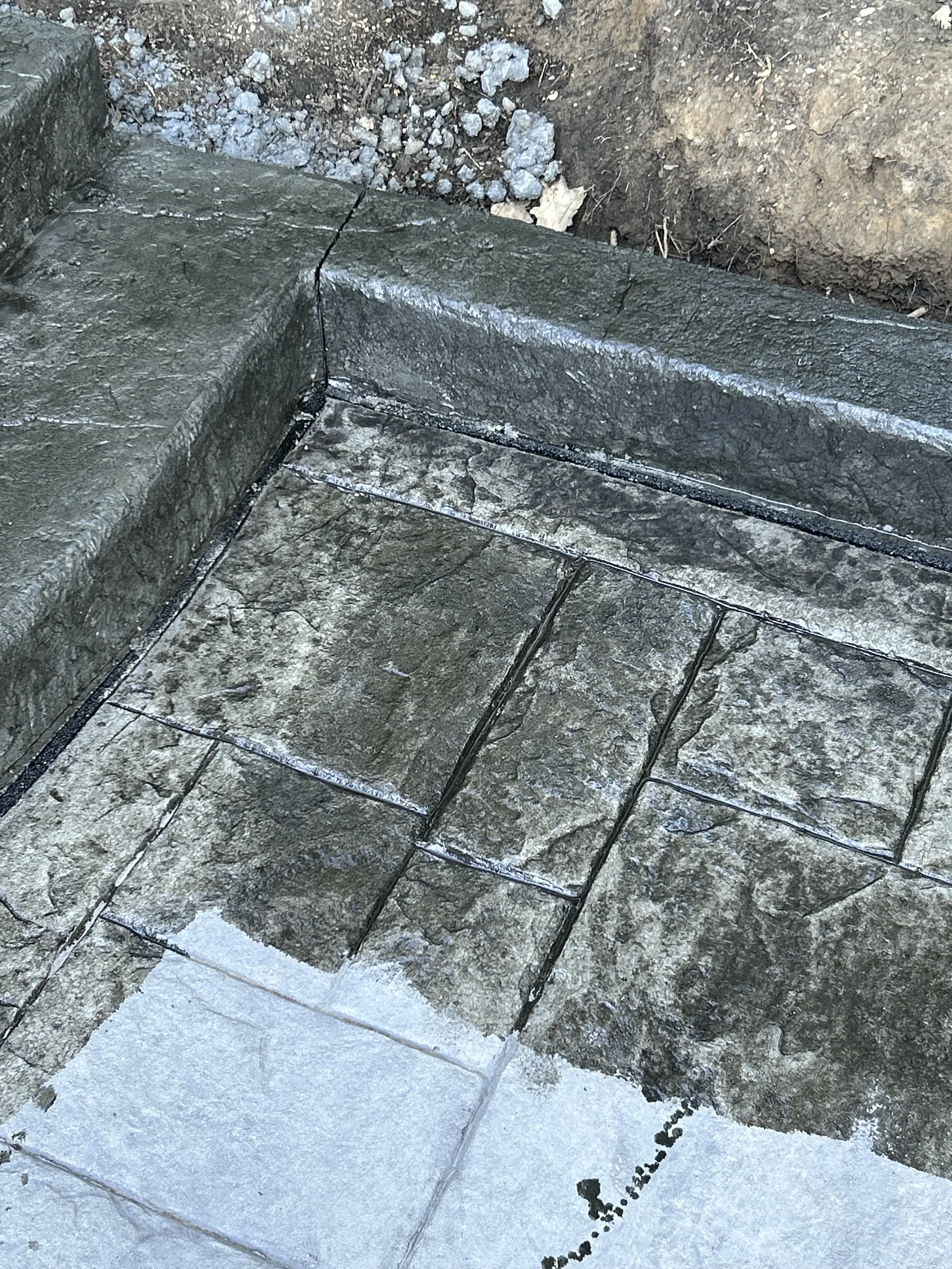 Close-up of a stone stair tread with a small pile of dirt and rocks beside it, with snow on the ground.