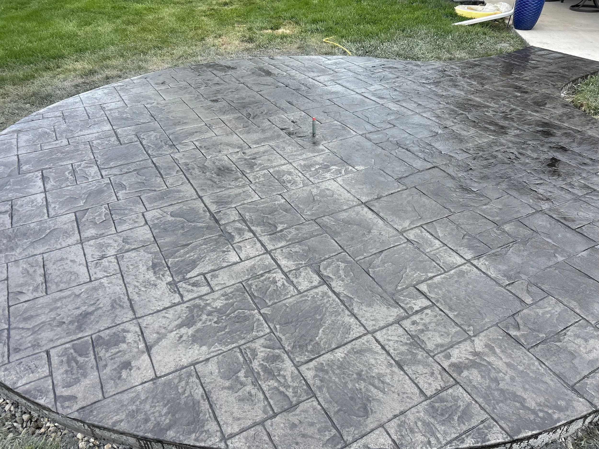 A newly paved concrete patio with textured gray stone pattern, freshly sealed.