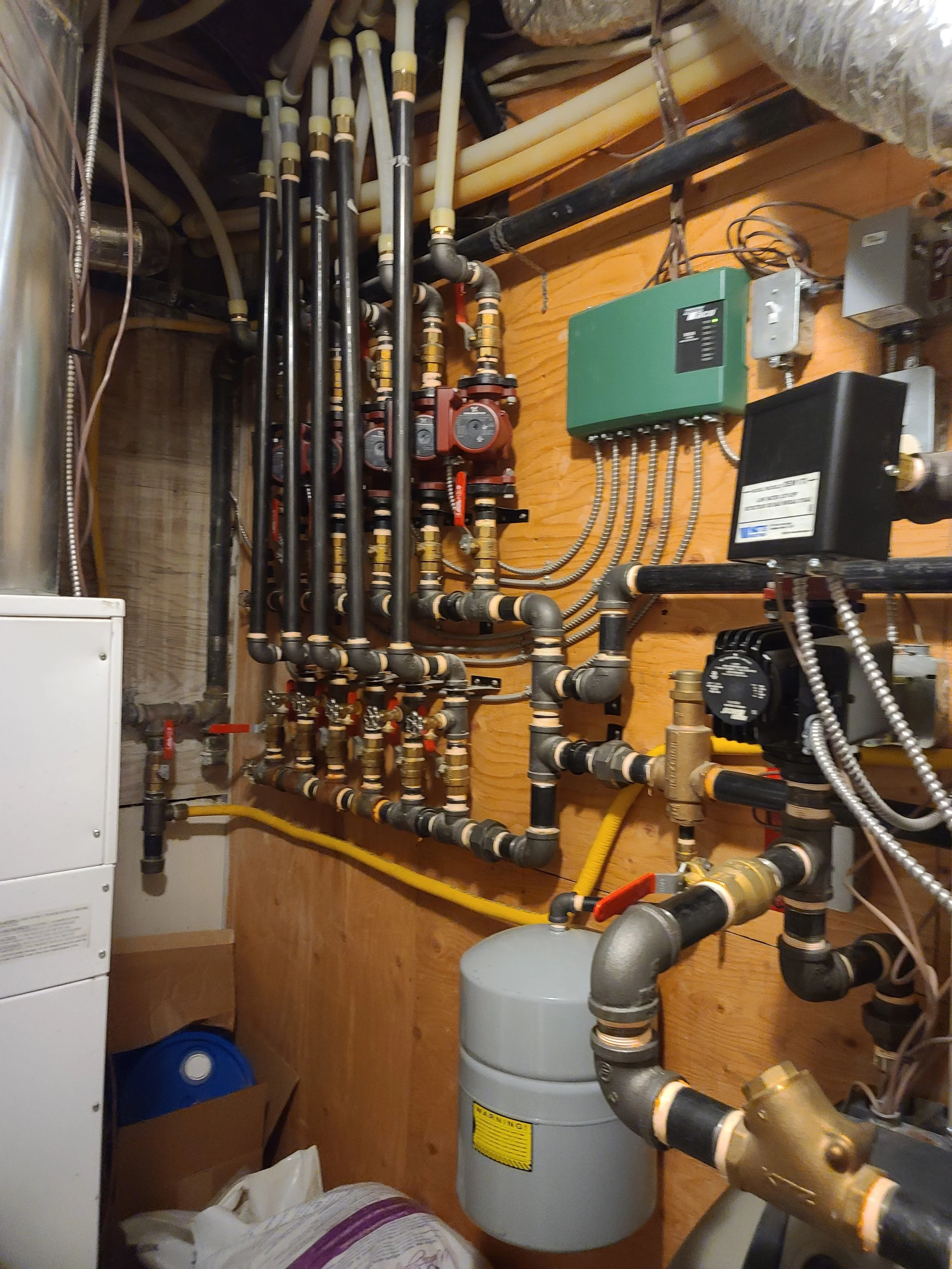 A mechanical room with plumbing pipes, an electric box, and a water heater.