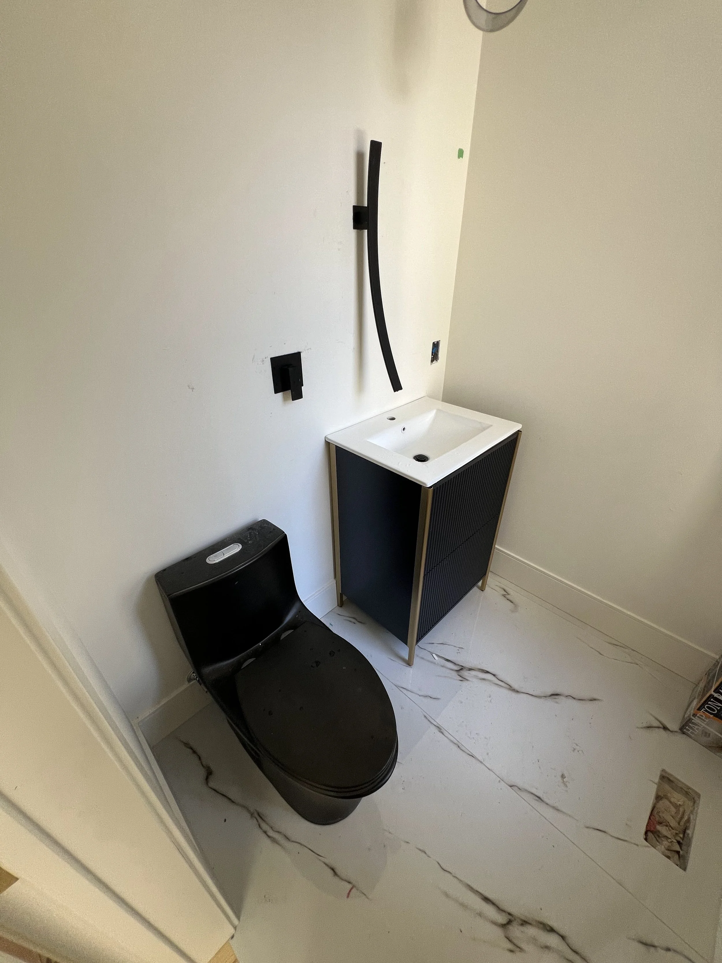 Bathroom with vanity, black toilet, and marble-like floor. Some wall fixtures are installed but not connected.