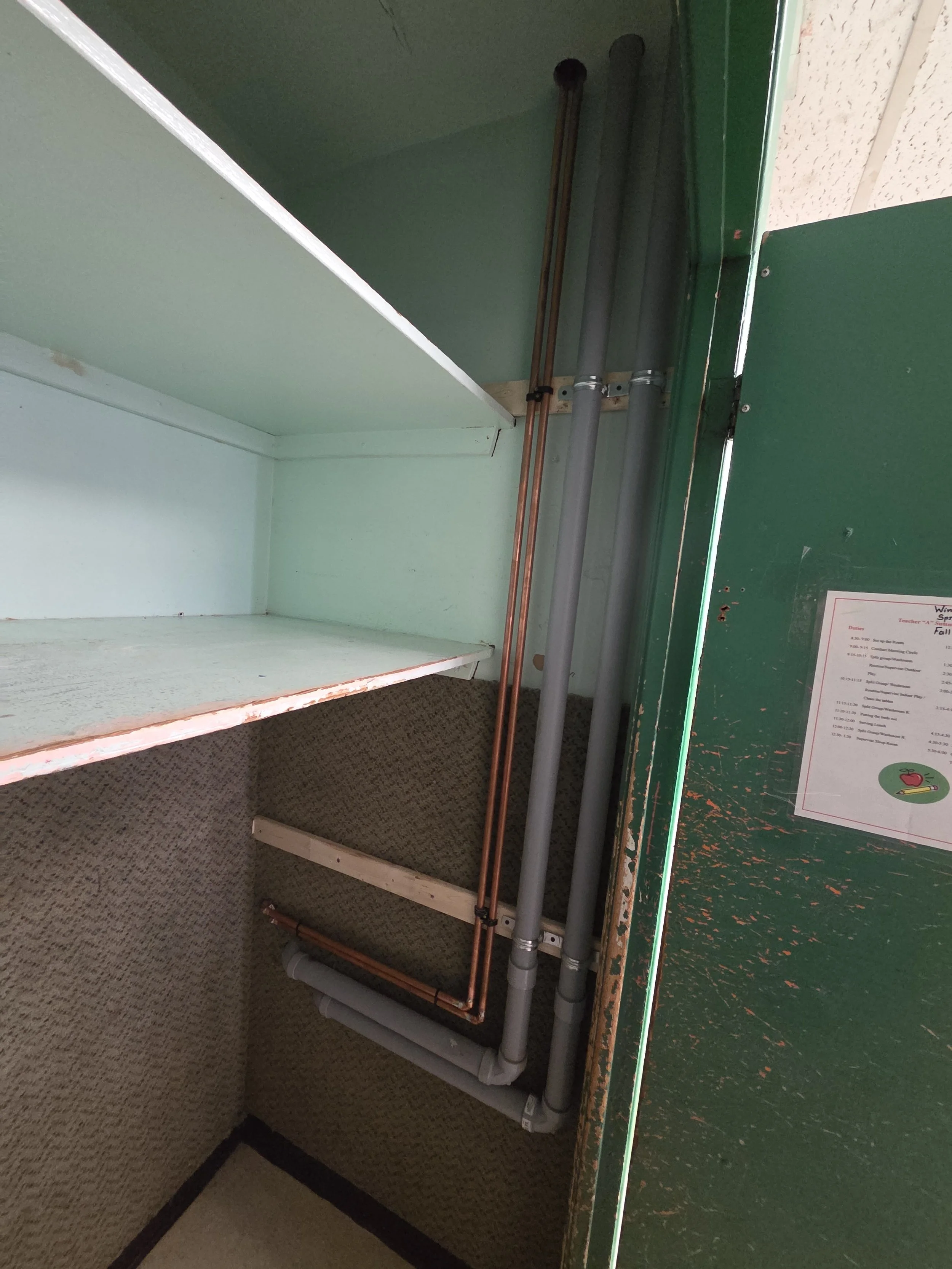 Empty green display case or shelf with pipes attached underneath, in a retail or storage area.