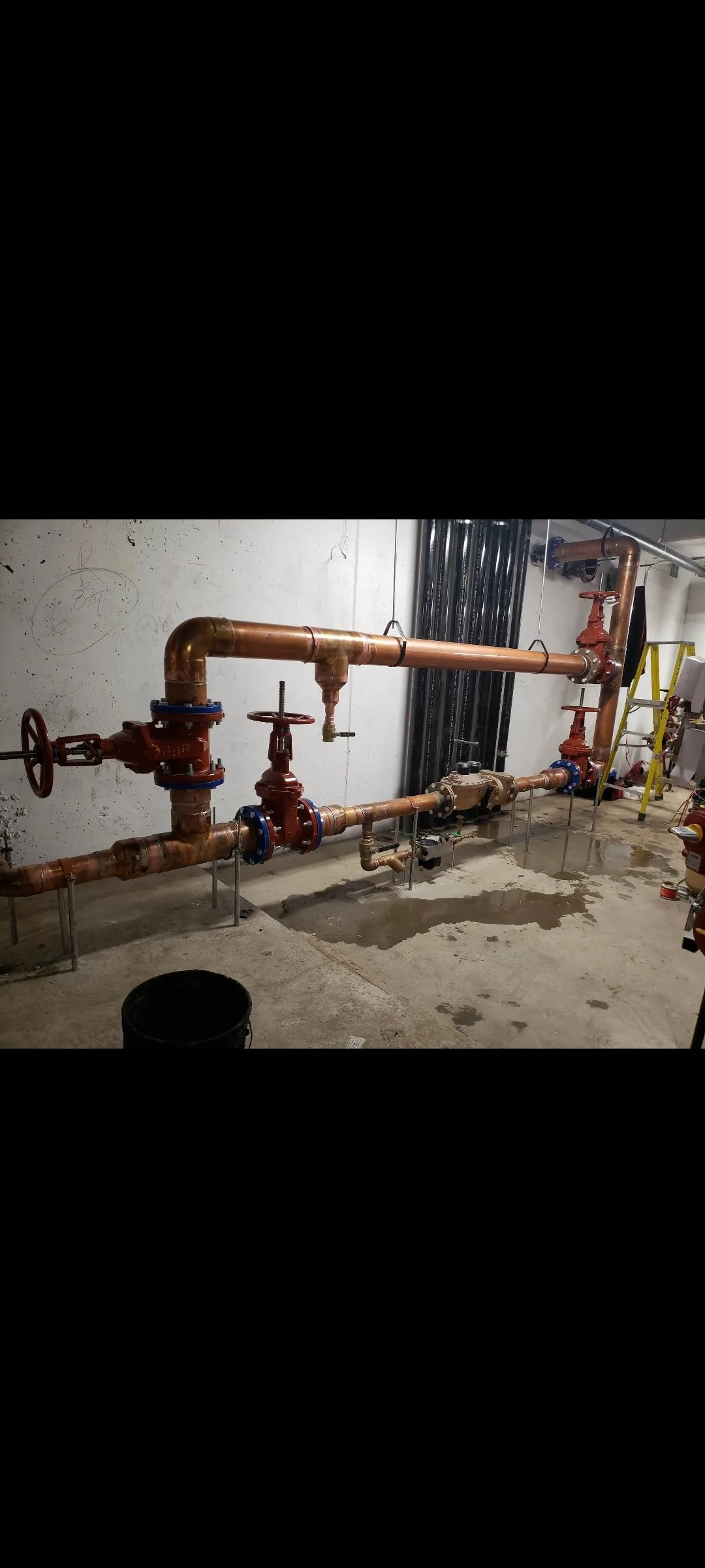 A network of copper pipes with red and blue valves installed on a concrete floor in a building under construction or maintenance.