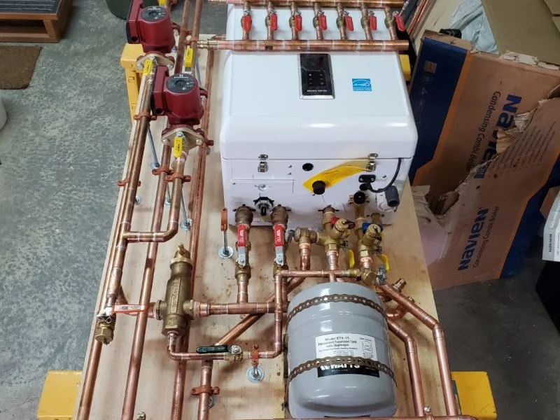 A plumbing setup with copper pipes, valves, and a water heater or boiler on a wooden surface.