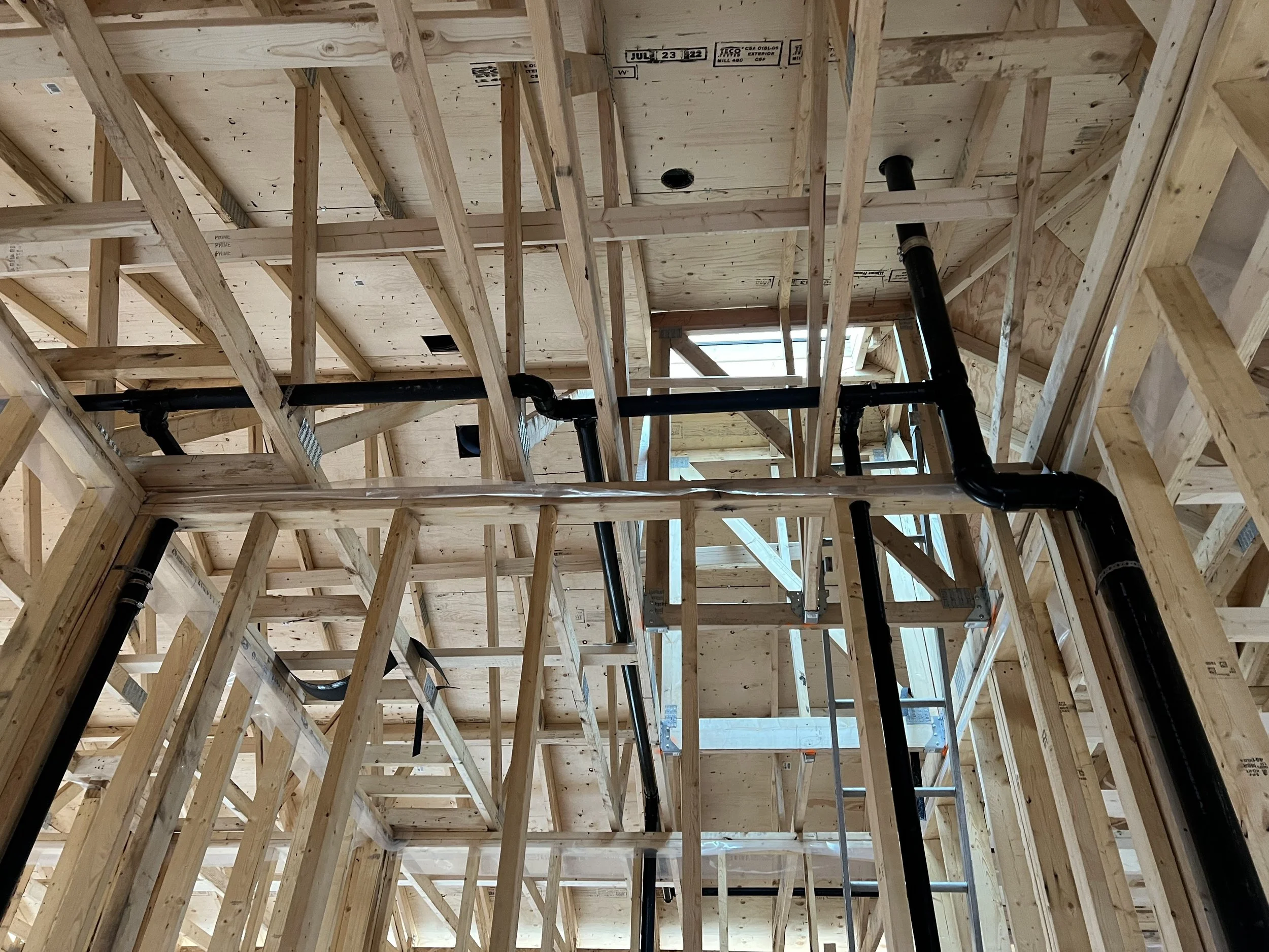 View of a building under construction with exposed wooden framing and plumbing pipes.