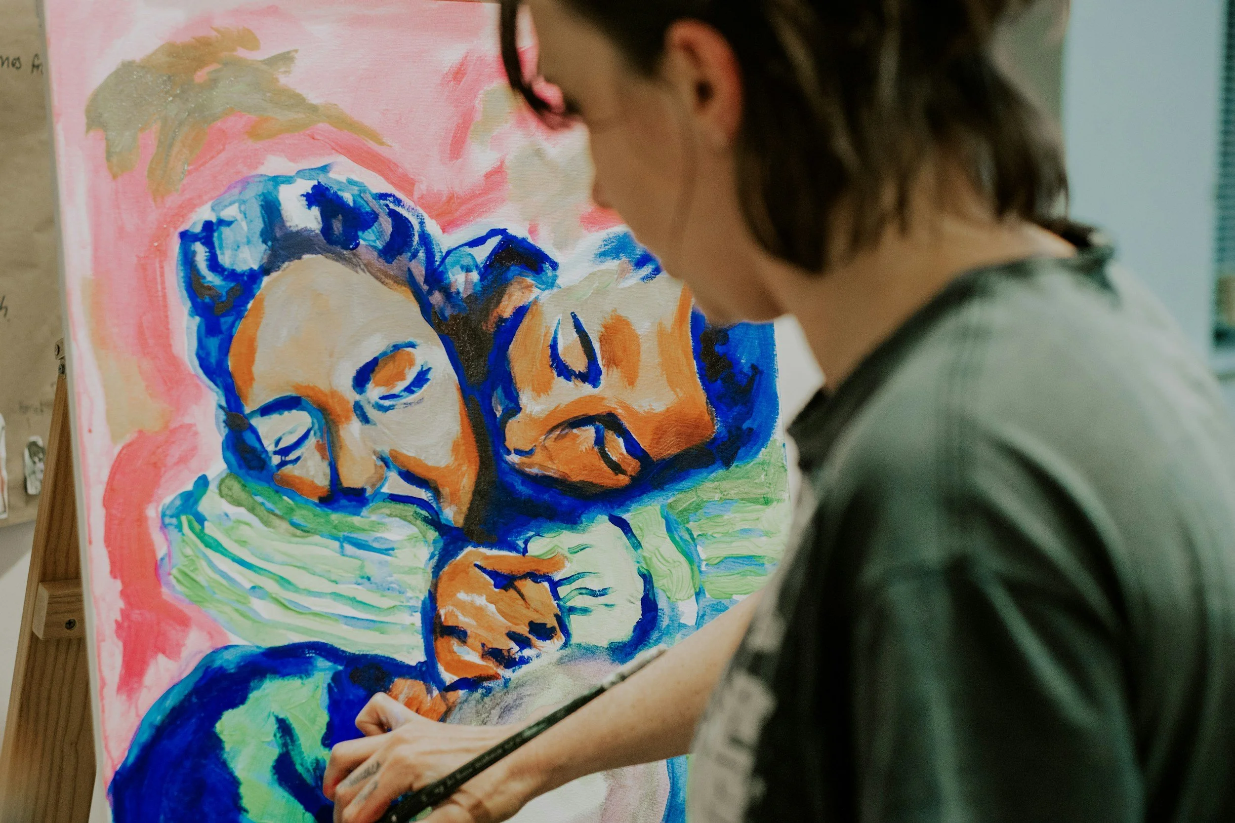 A person painting a colorful, abstract portrait of a woman with short hair on a canvas.