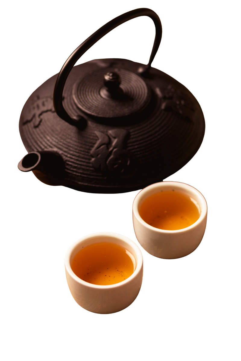 A black cast iron teapot with a handle and two white ceramic cups filled with tea.