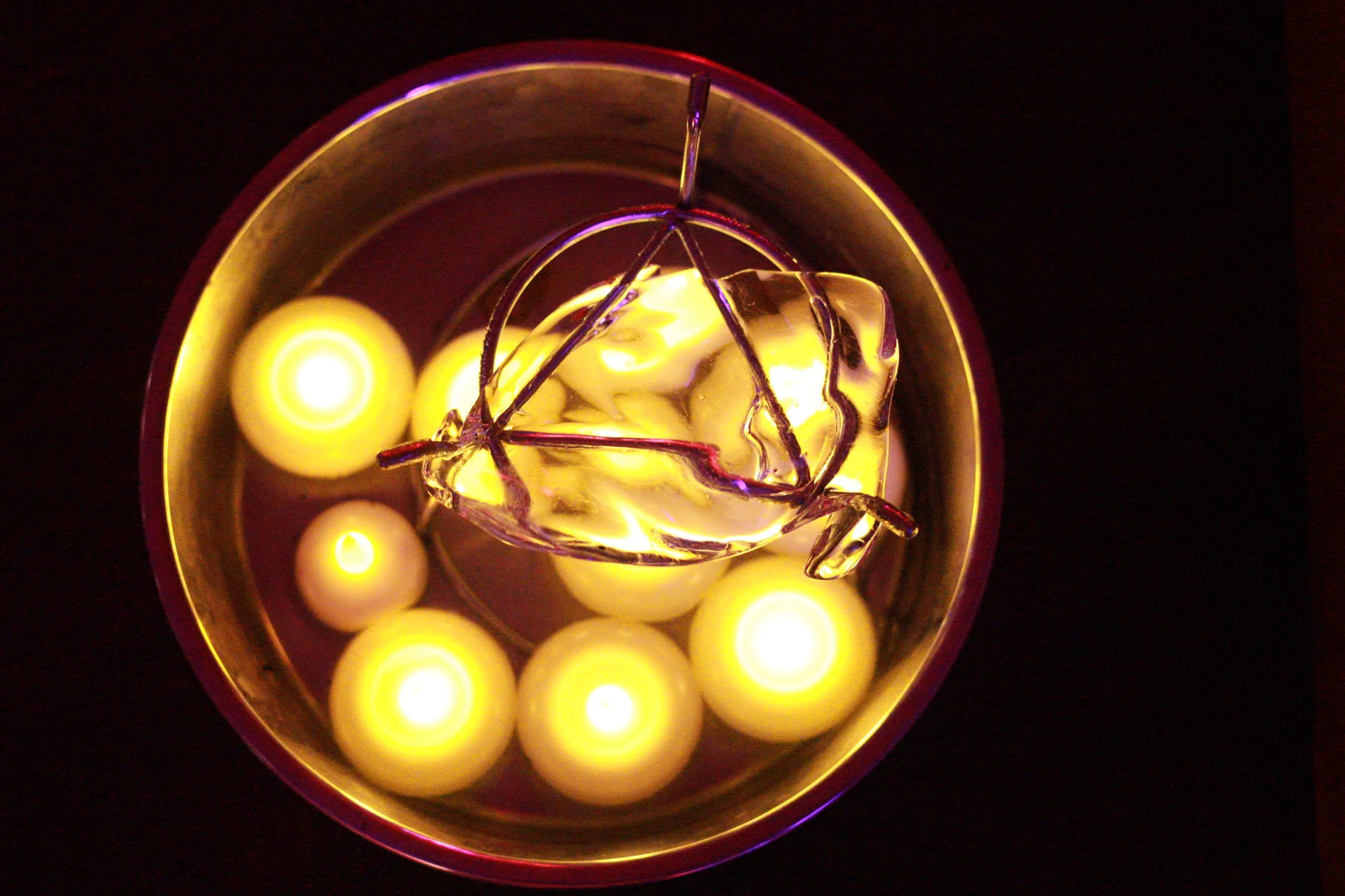 Close-up of a glass container with a metal star-shaped ornament and yellow candles, some lit, reflecting inside