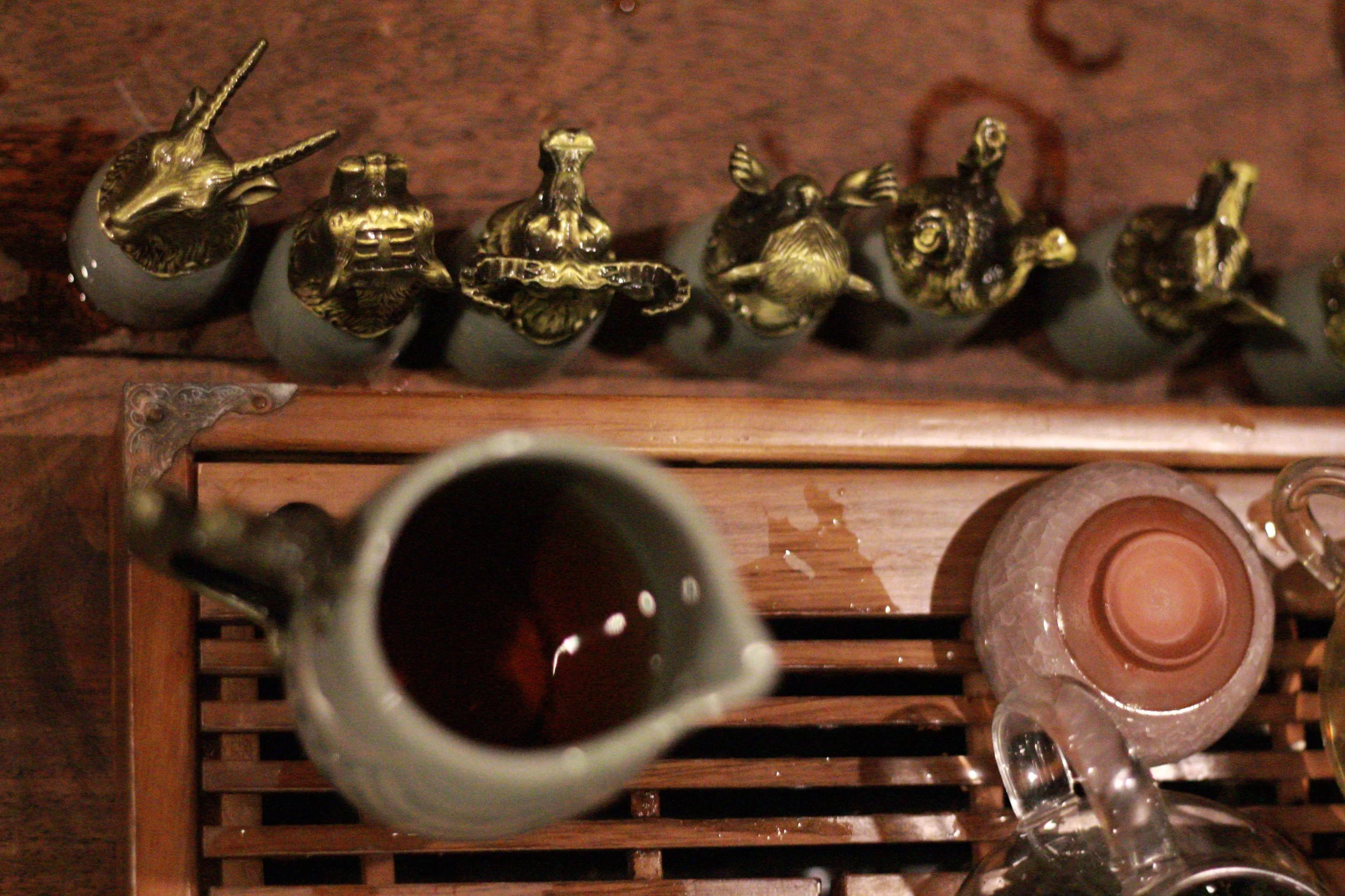 Overhead view of a row of intricately carved vintage silver and brass doorknockers on a wooden surface, with glasses and mugs nearby.