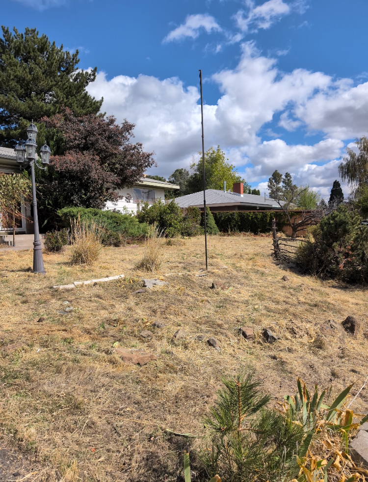 A Klamath Falls residence  with the yard timmed back, trees, shrubs, a house with a gray roof, and an old-fashioned street lamp, under a partly cloudy sky.