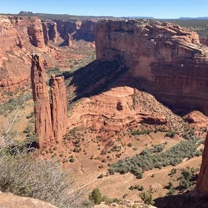 Red rock canyon landscape with tall cliffs and rock formations under a clear blue sky.
