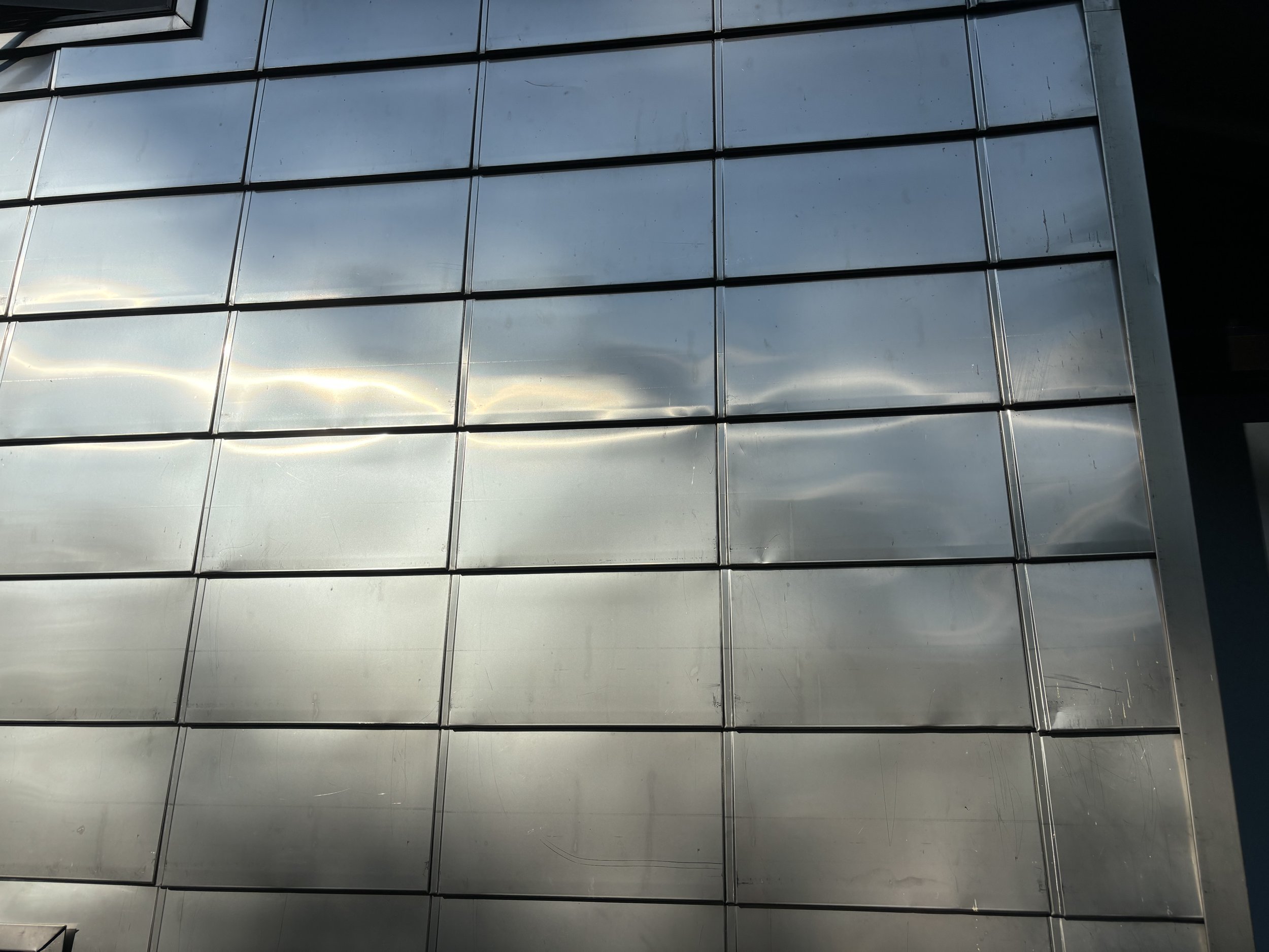 Reflection of clouds and sky on a modern stainless steel facade with horizontal and vertical metal framing.