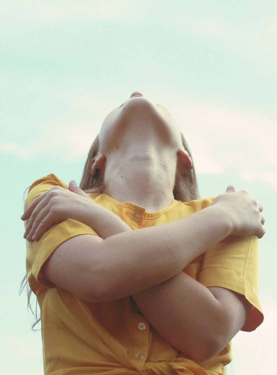 Woman in yellow hugging herself representing the emotional blocks and inner resistance that stop entrepreneurs and solopreneurs from taking action and scaling their business