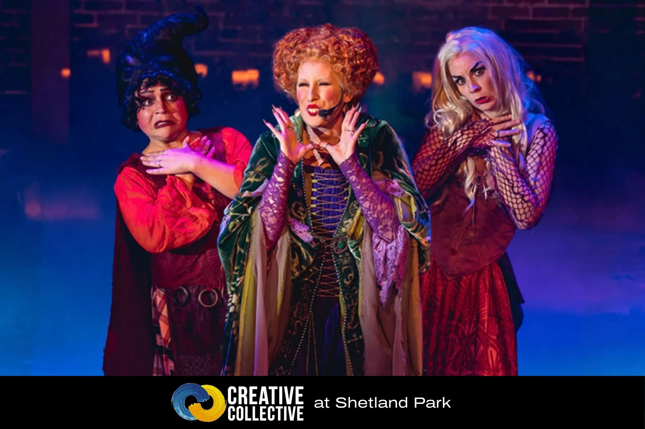The Sanderson Sisters live on stage in Salem MA during a product of Rock Cauldron Cabaret. The sisters stand in typical poses while smoke and lit candles surround them.