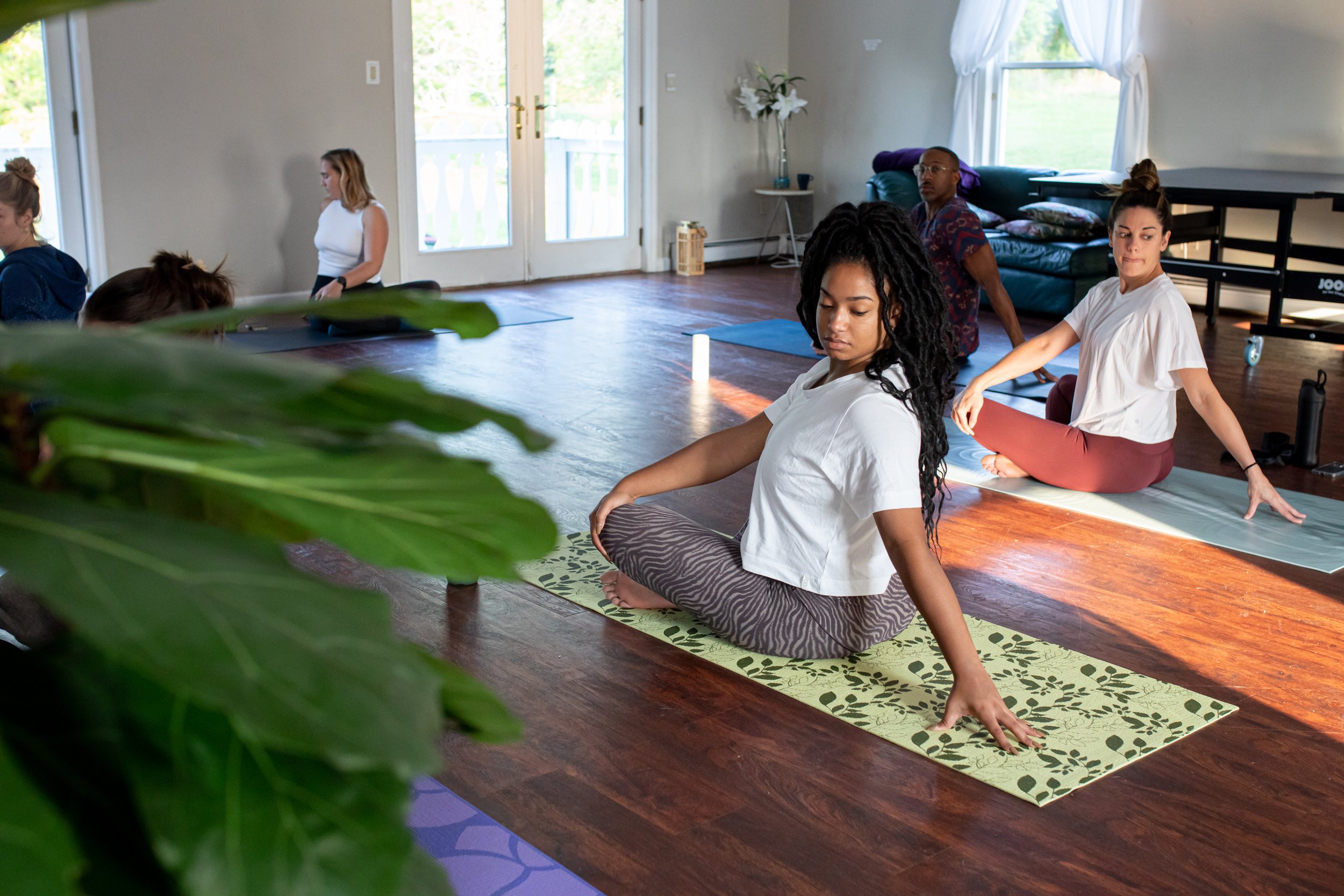 People participating in a yoga or meditation class indoors, sitting on yoga mats in a cross-legged position with eyes closed or focused.