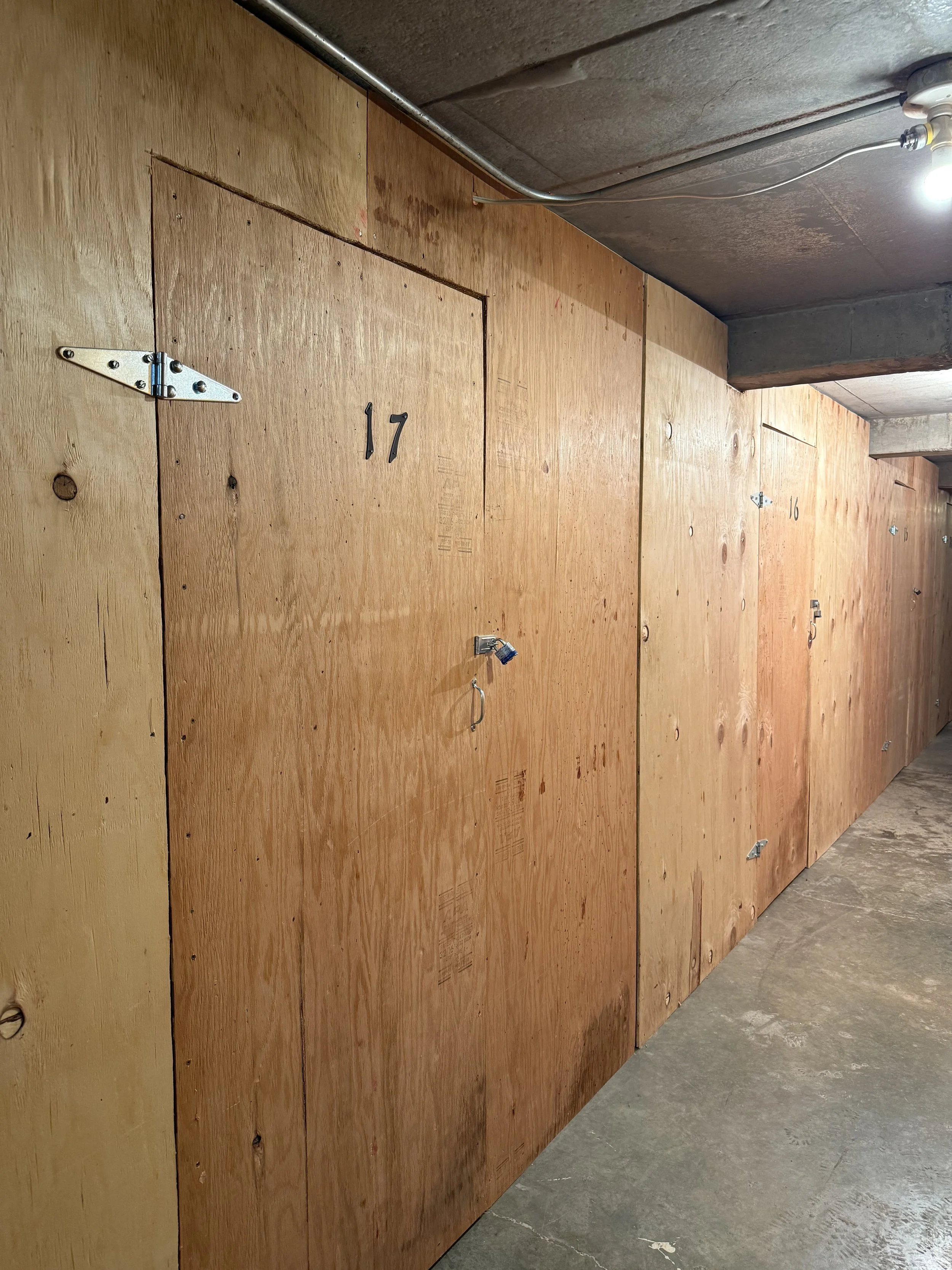 Indoor storage area with plywood walls and numbered lockers, including locker 17 and 16, with some locks and hardware visible.