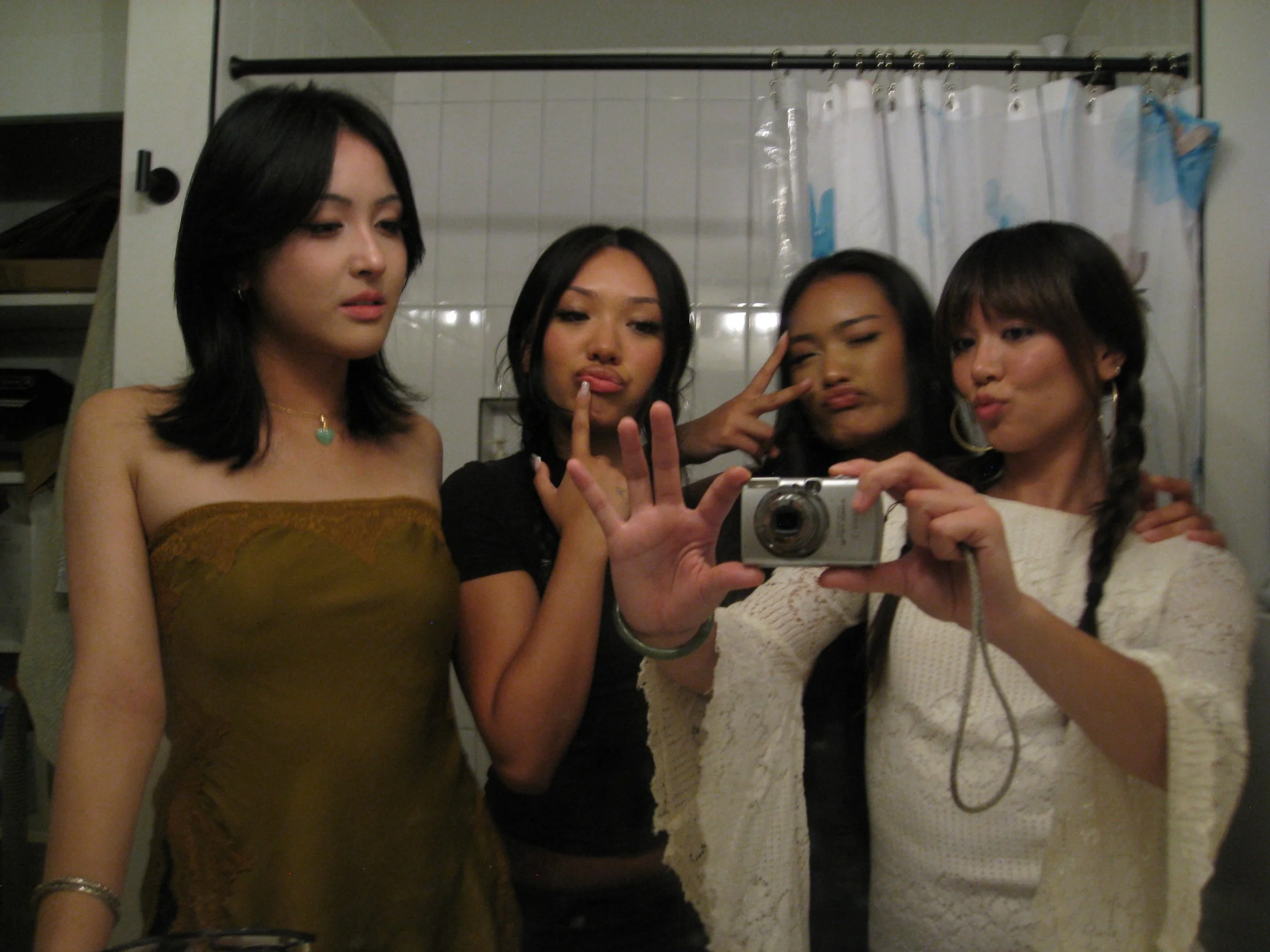 Four women taking a mirror selfie in a bathroom. They appear to be posing and making expressive faces.