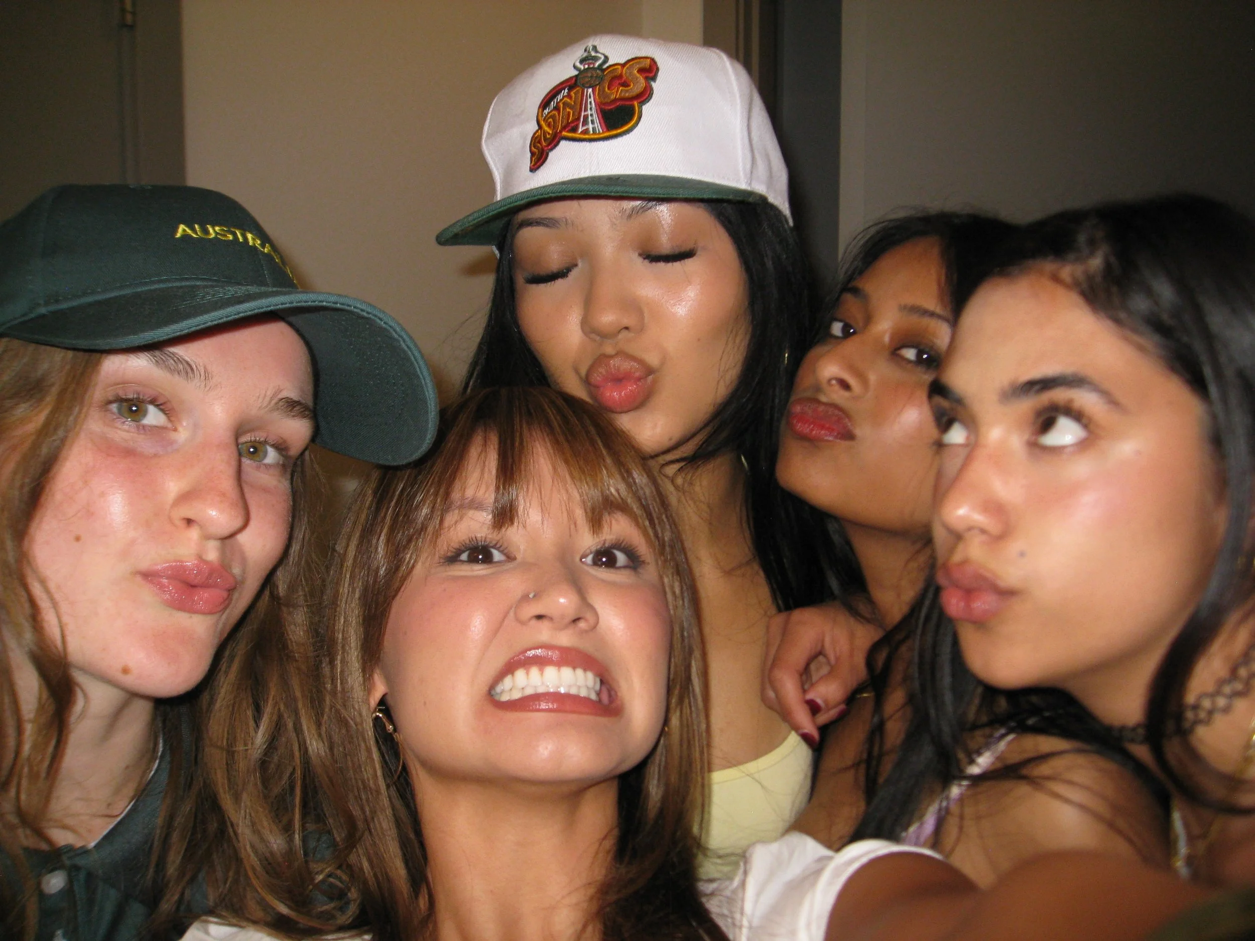 Close-up of a diverse group of young women taking a selfie together, displaying various facial expressions and wearing casual clothing and accessories.