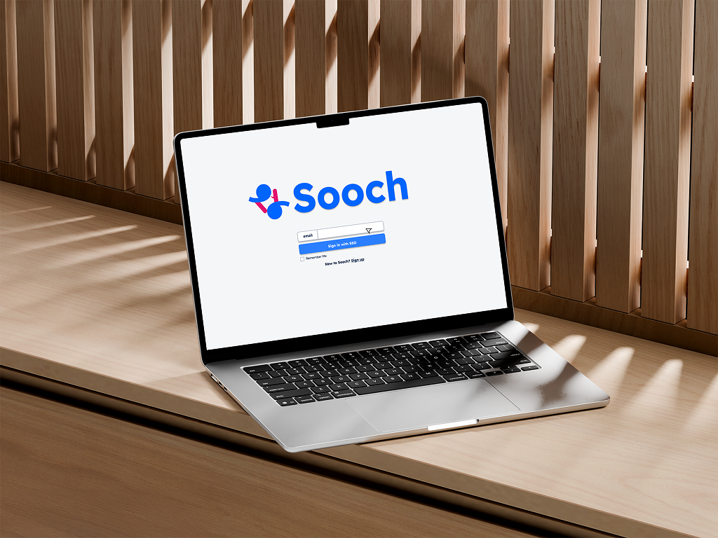 Open laptop on a wooden desk displaying the Sooch login page on the screen, with a wooden slat wall in the background.