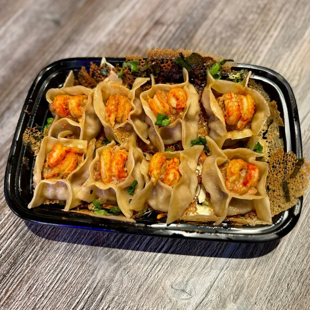 Tray of dumplings topped with small pieces of cooked shrimp, garnished with chopped green onions, on a wooden surface.