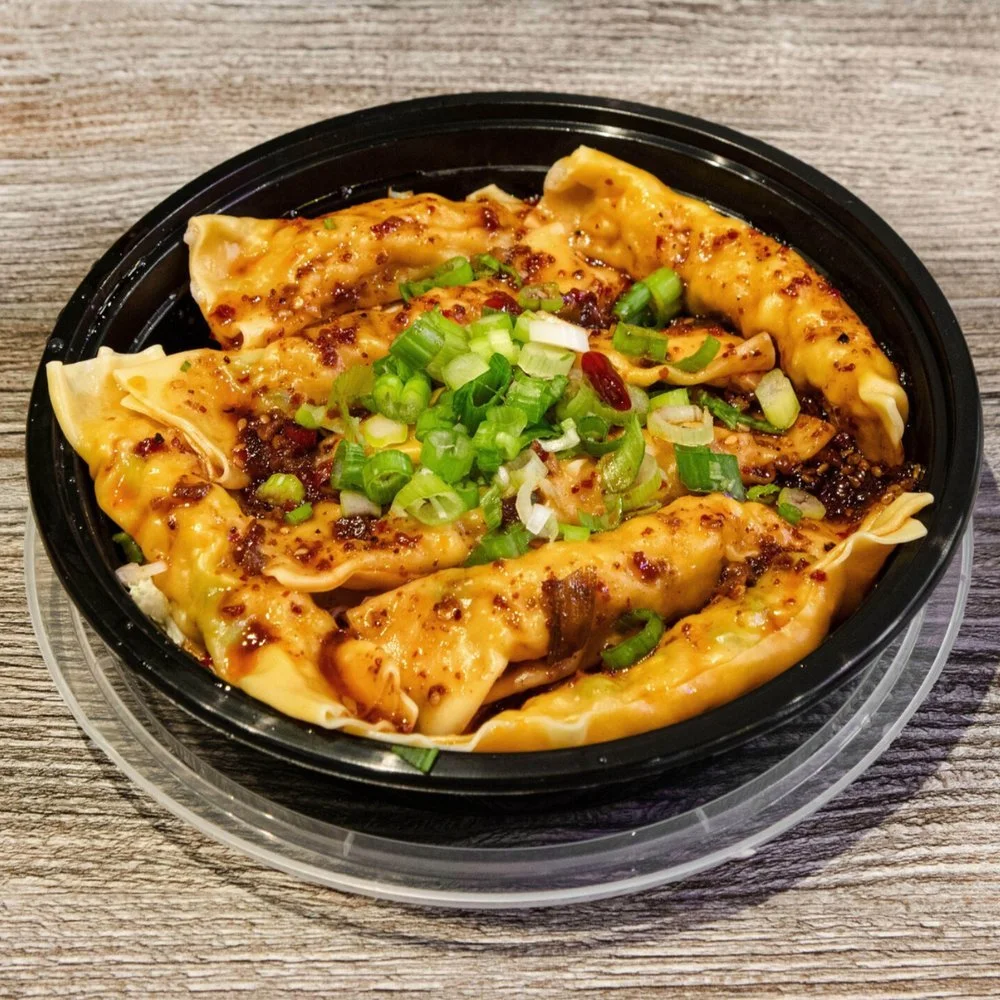 Close-up of a black plastic container of Chinese dumplings garnished with chopped green onions, on a wooden table.