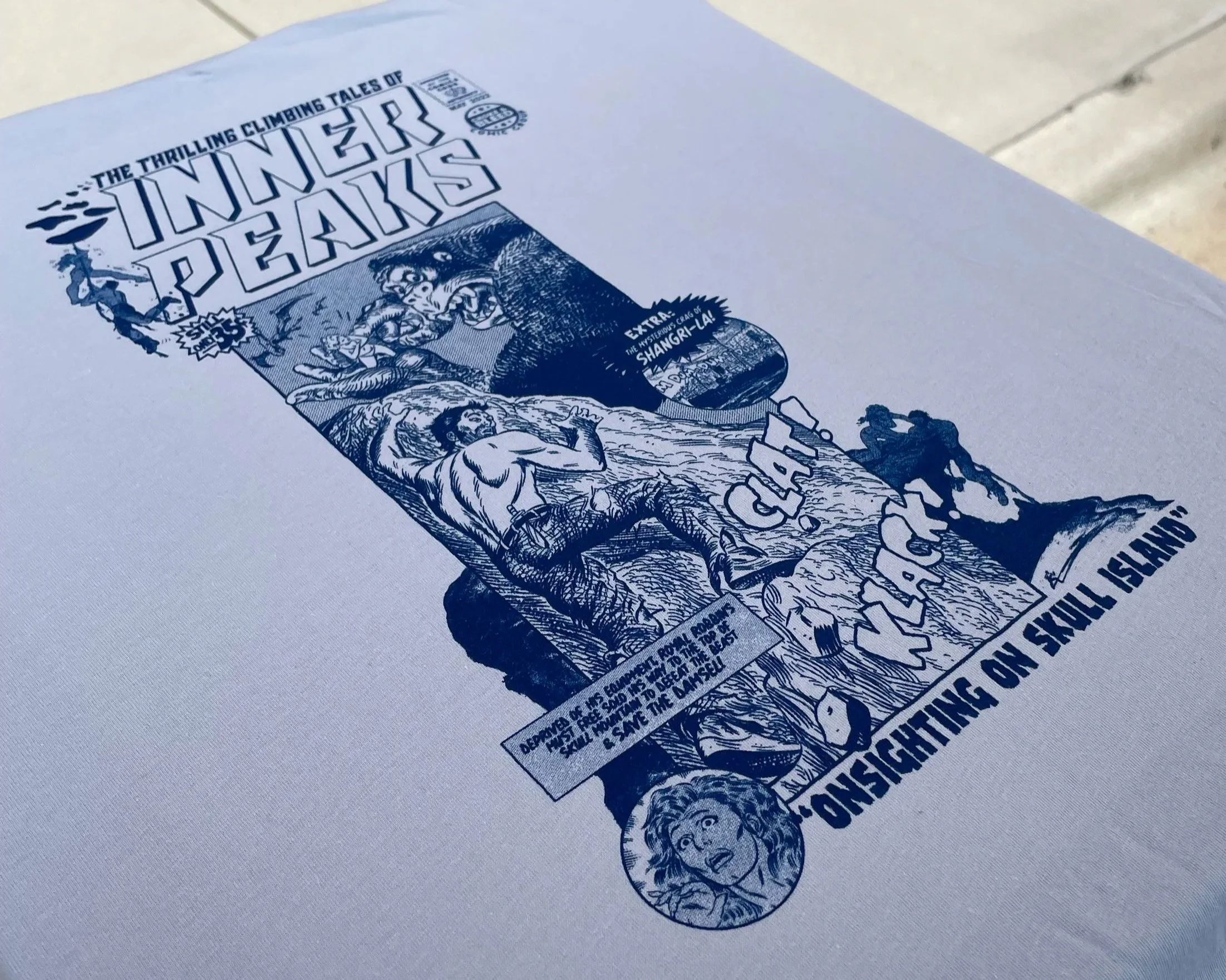 Close-up of a printed flyer advertising an event called 'Inners Peaks' with stylized text, illustrations of people climbing, and a mountain scene, all in blue ink on white paper.