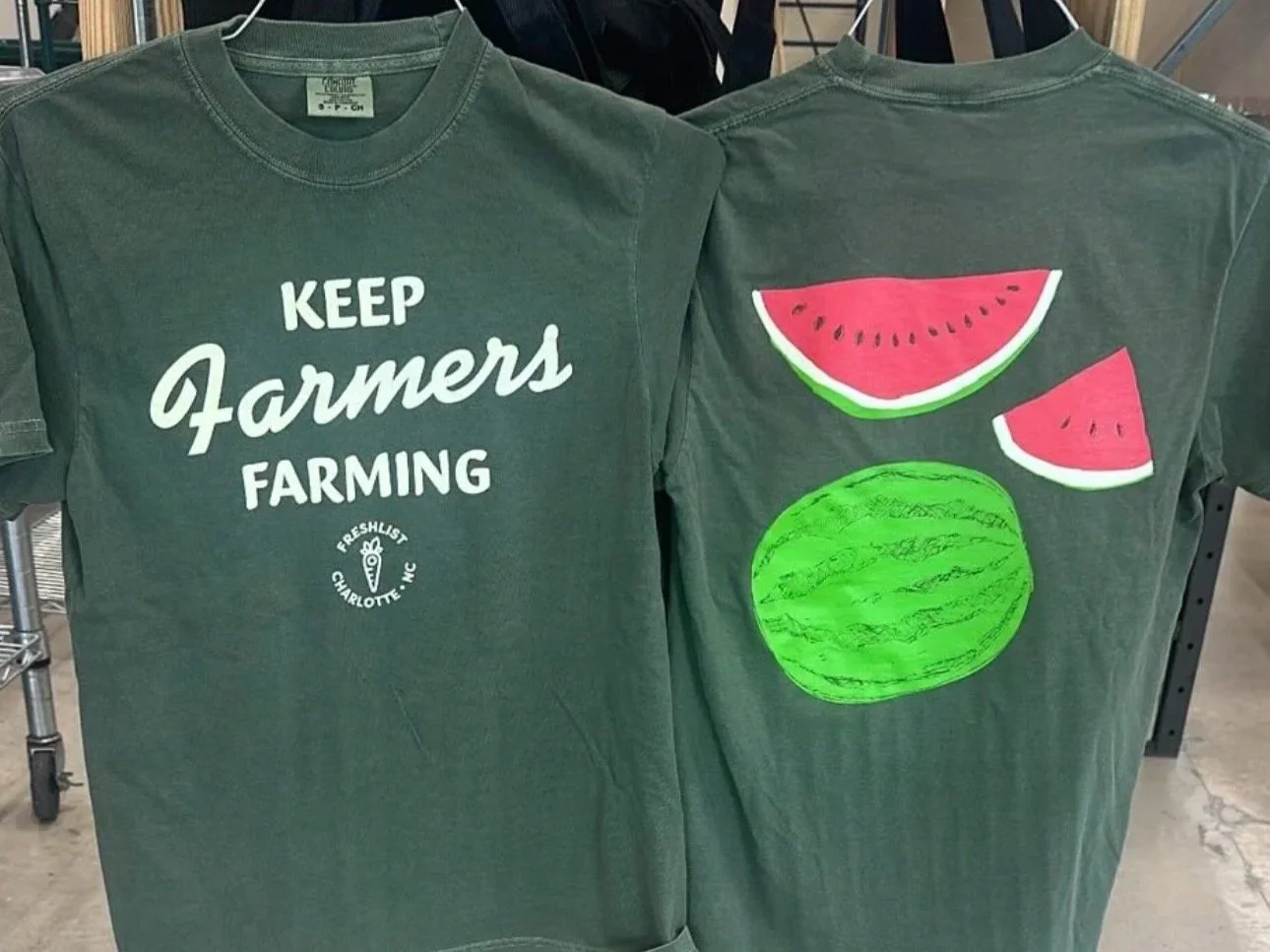 Two green T-shirts displayed side by side, one with the text 'Keep Farmers Farming' and a small carrot graphic, the other with illustrations of a whole watermelon and slices of watermelon.