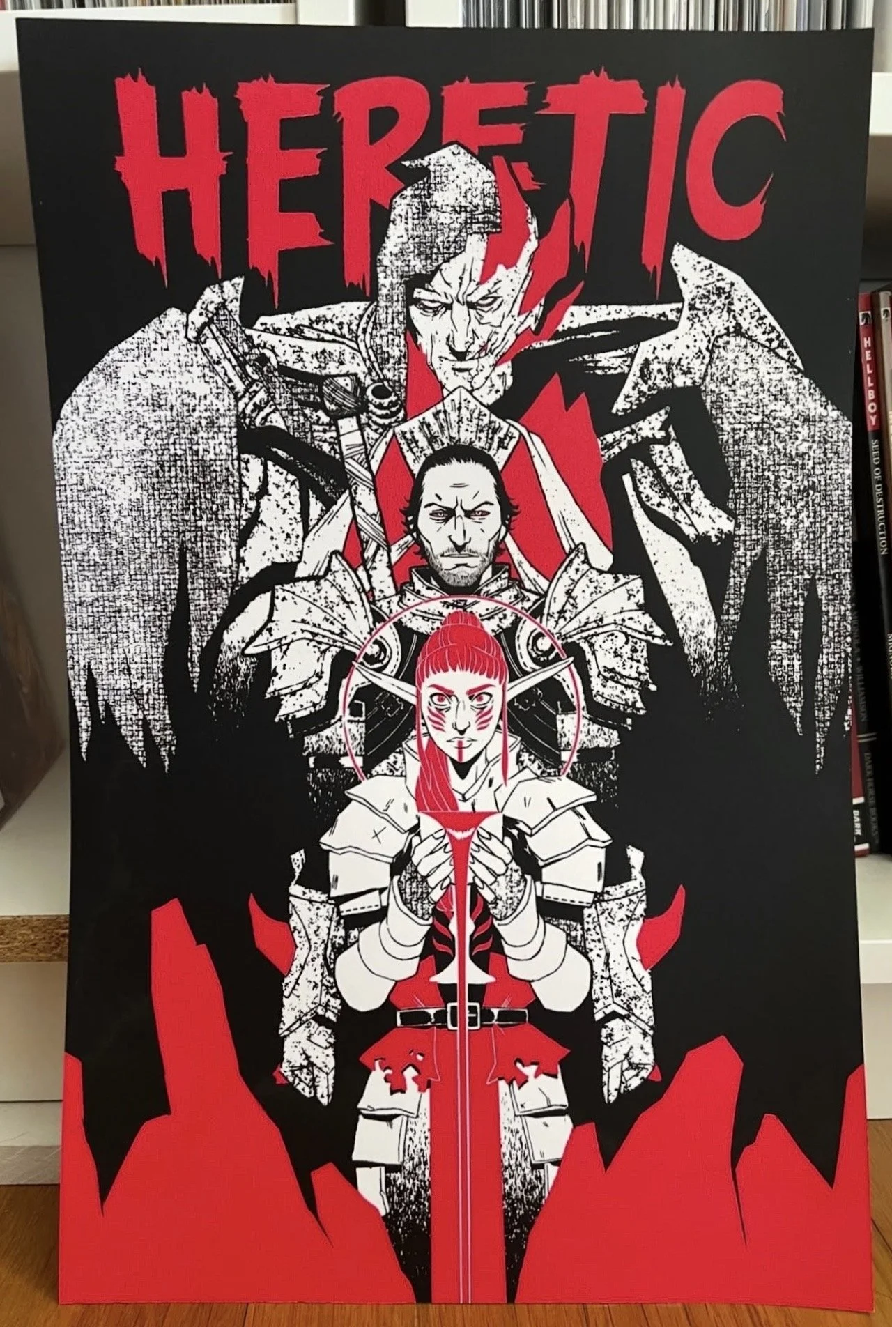 A black and red illustration of three characters from the movie 'Heretic.' The top character has a stern face with a pointed beard and warrior armor. The middle character is a dark-haired man with a serious expression, holding a sword vertically, and