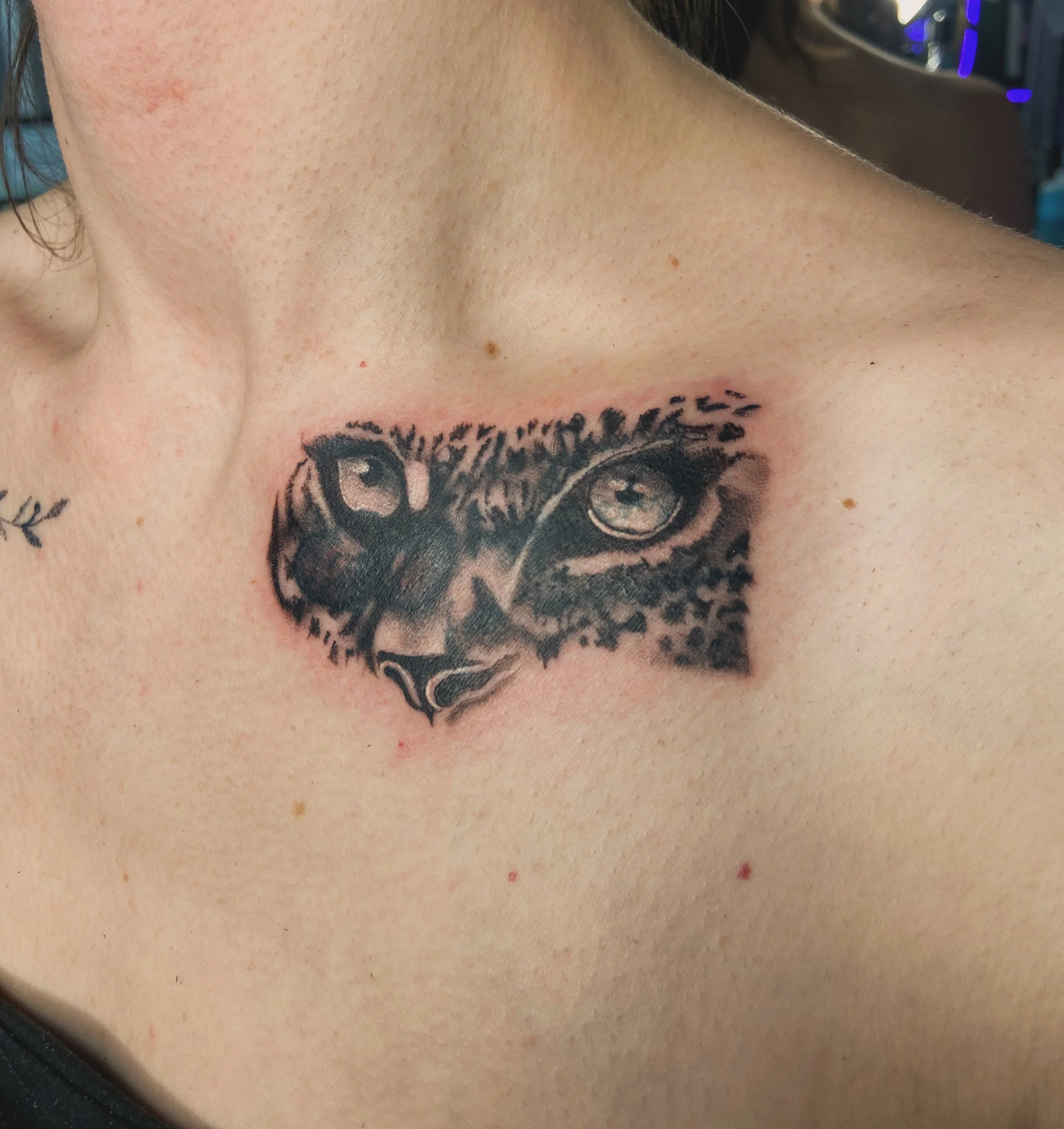 Close-up of a person's neck and shoulder with a tattoo of a cat's face and eyes.
