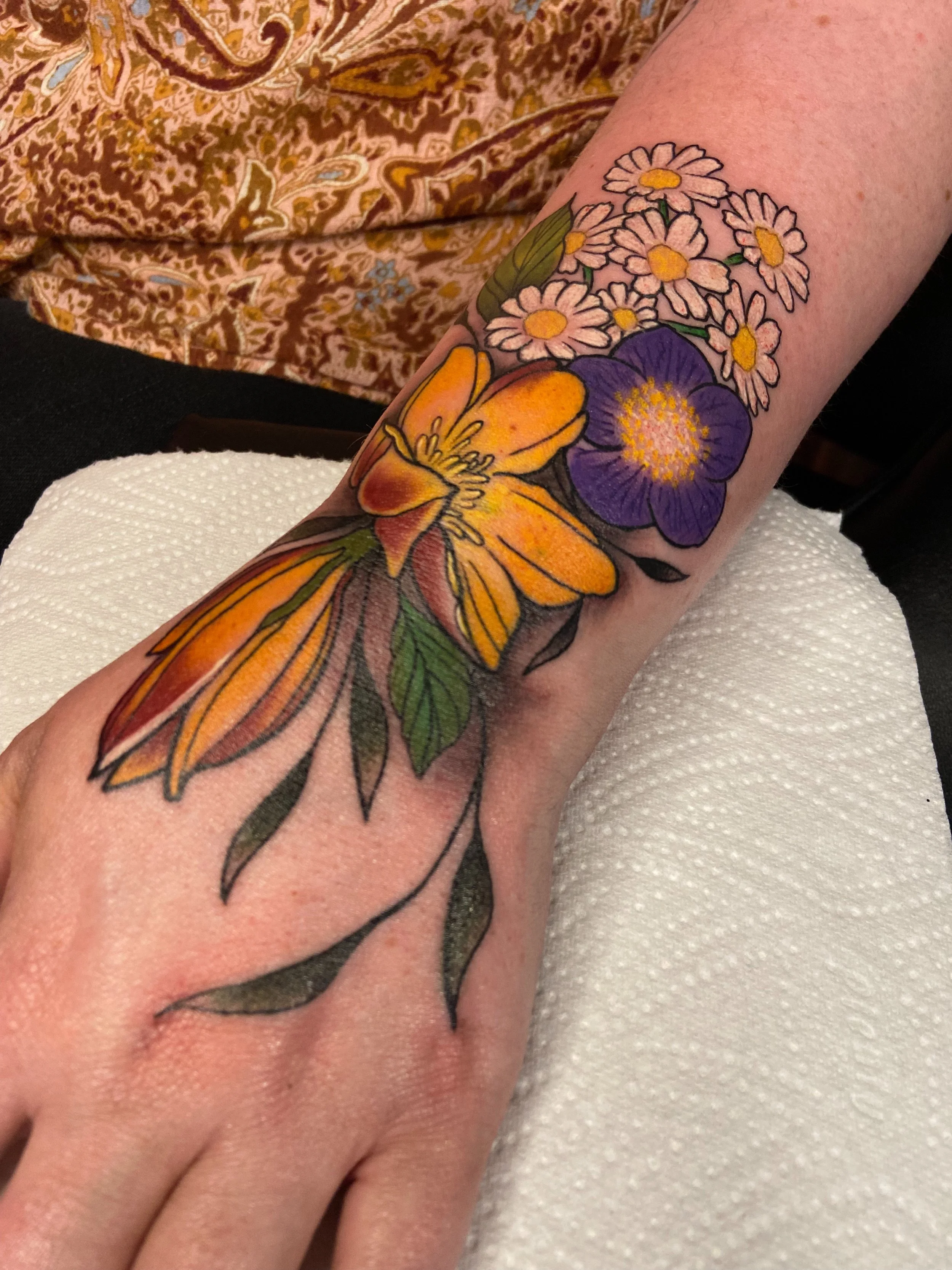Colorful tattoo of yellow and purple flowers on a person's forearm.