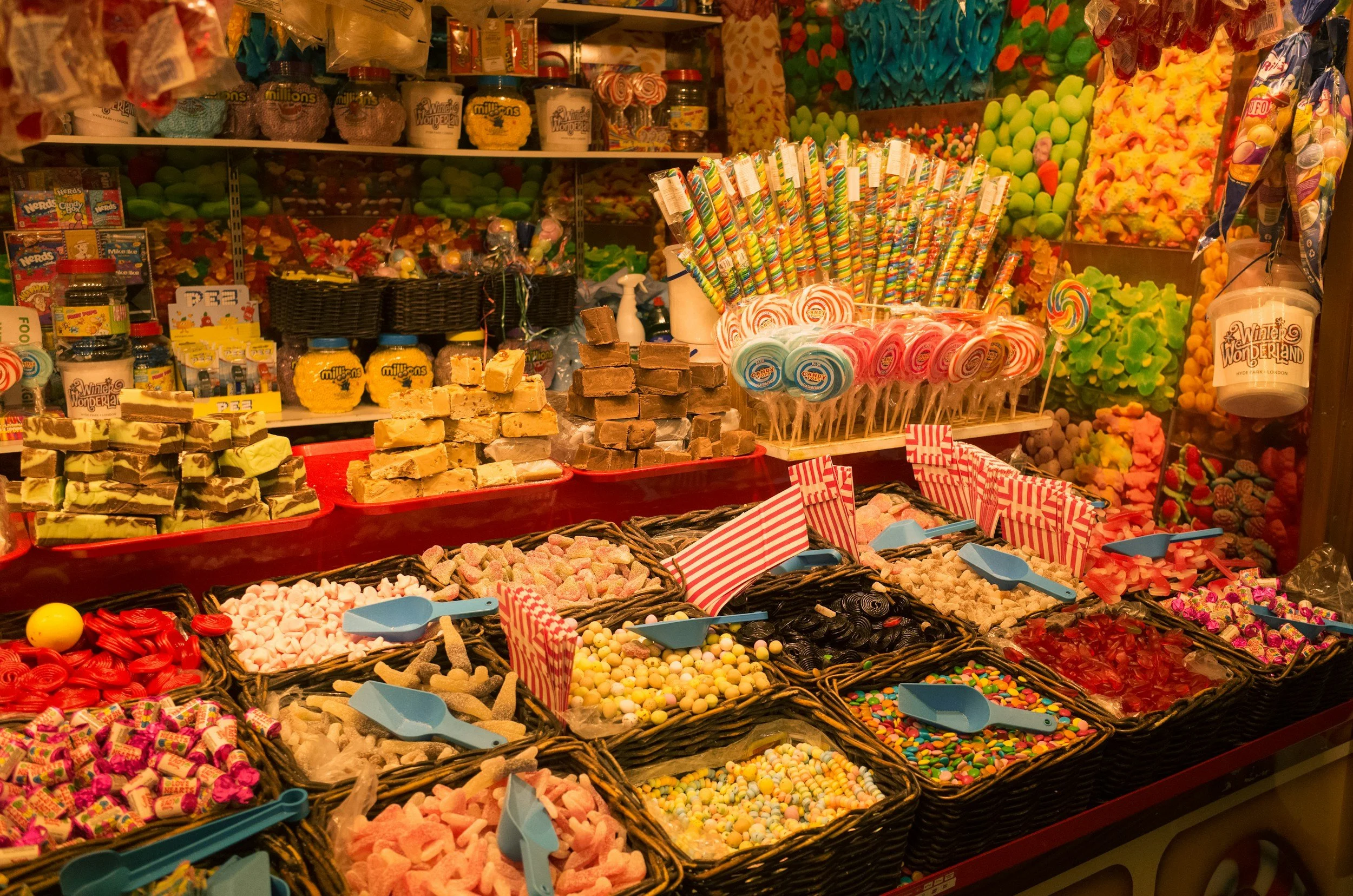 A retail display of assorted candies including gummies, chocolates, lollipops, and colorful sweets in baskets and containers.
