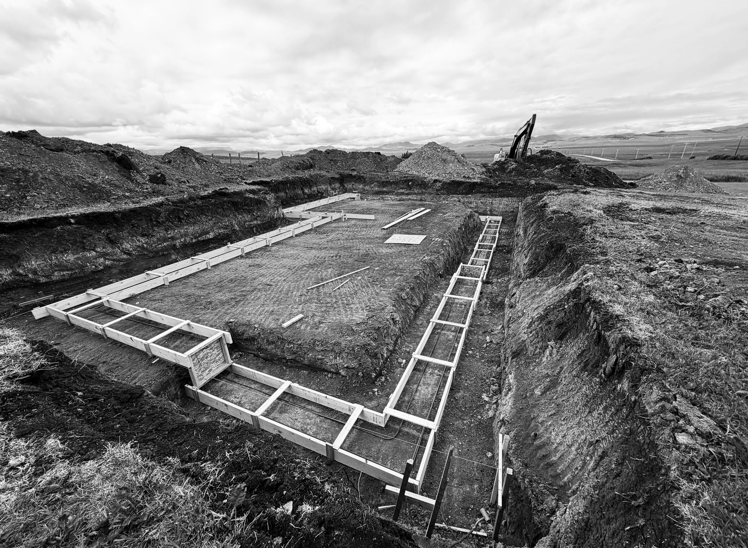 Construction site in an open landscape with an excavator and wooden framing for a foundation.