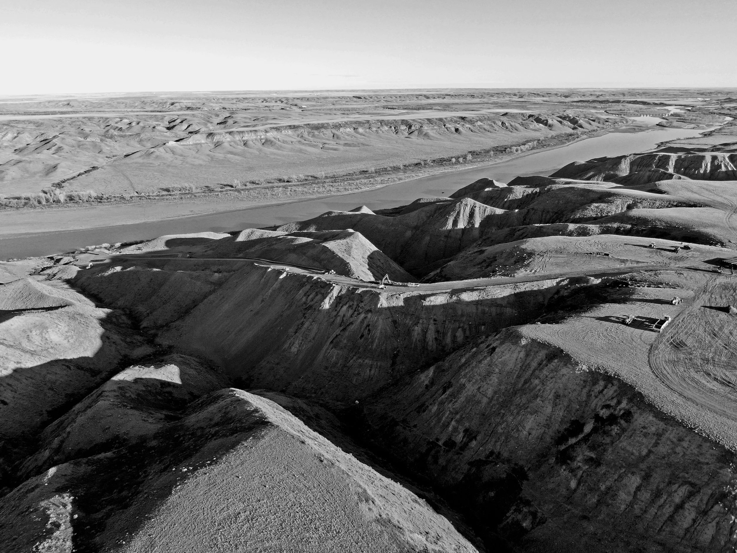Black and white aerial view of a rugged, hilly landscape with a road being excavated.