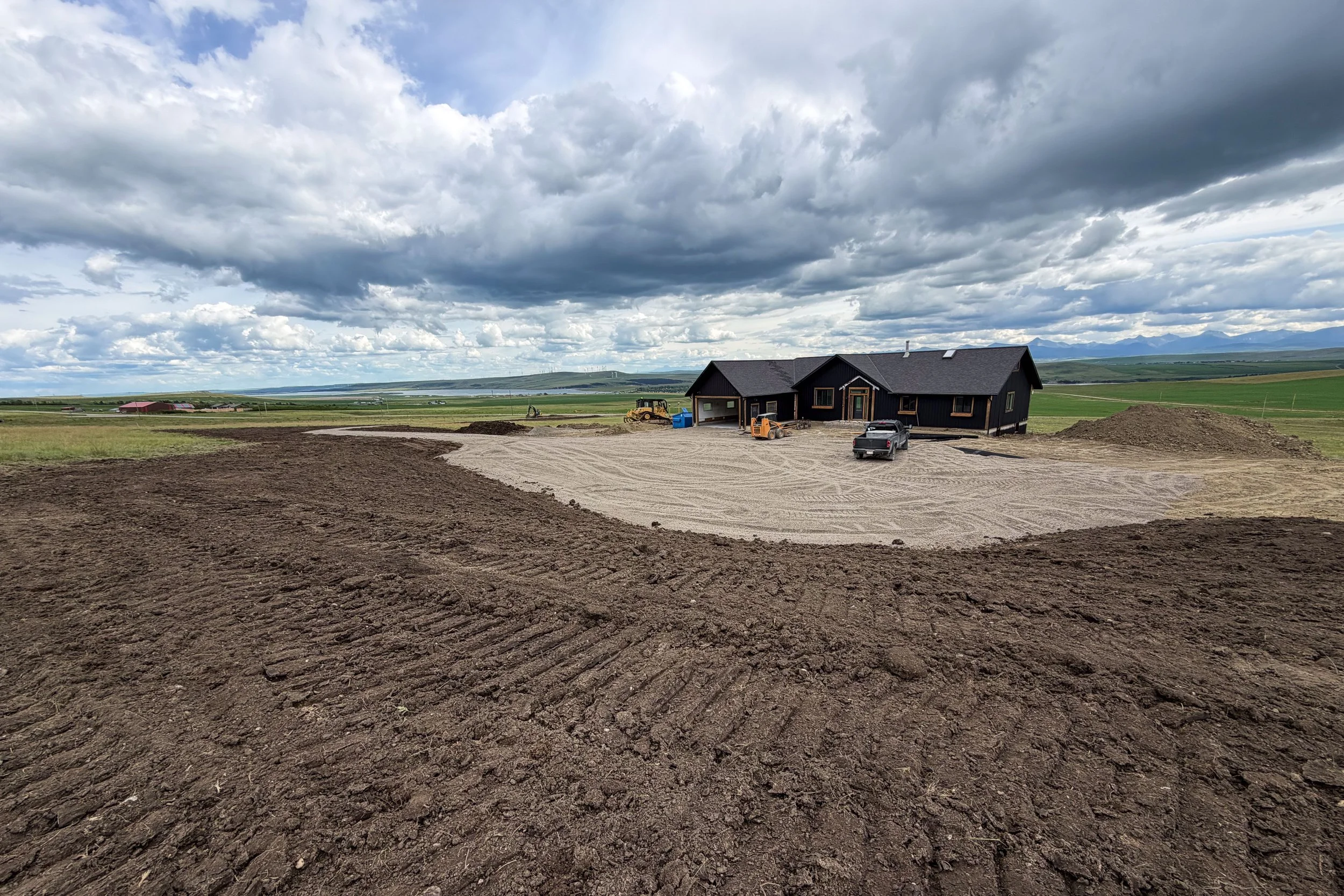 A house under construction in Southern Alberta with construction heavy equipment around it, acreage site being developed with proper drainage and geotech matting.
