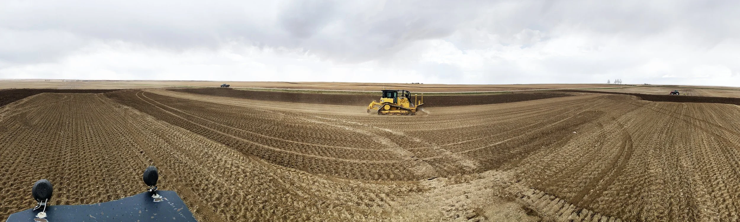 A yellow bulldozer working on a large, open farmland with freshly landscaped soil.