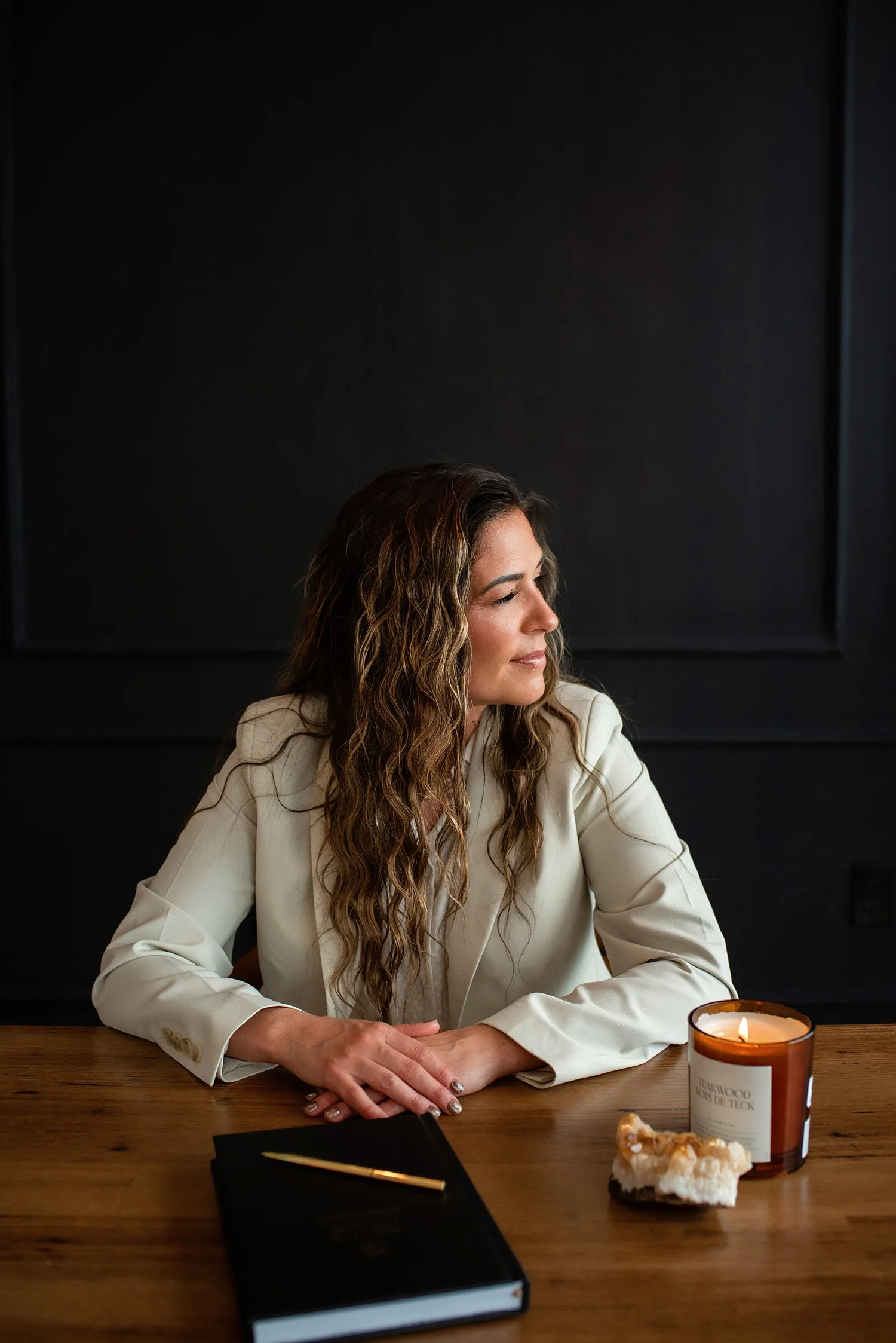 Chantal Menard in a light-colored blazer sitting at a wooden table, with a lit candle and some bread in front of her, against a dark background.