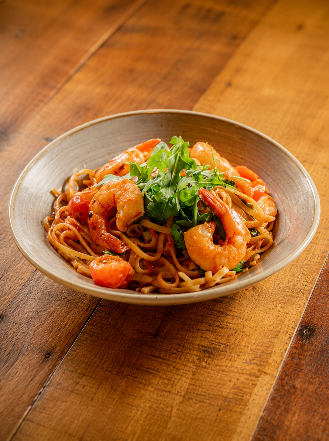 Shrimp pasta with cherry tomatoes and fresh arugula on a wooden table.