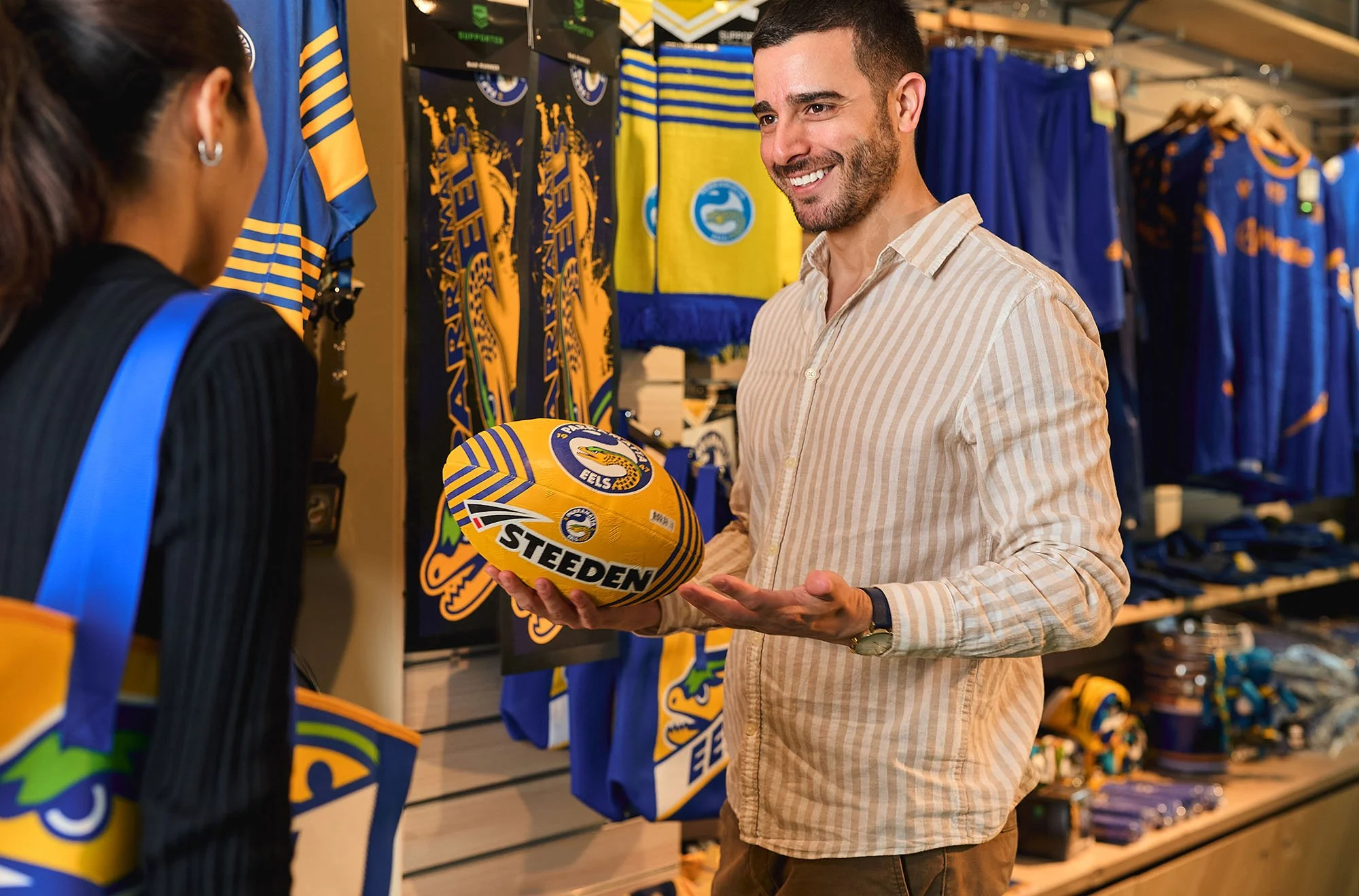 Black fleece jacket with the words "PARAMATAS TEs" embroidered in yellow and blue, hanging on a rack in a clothing store.
