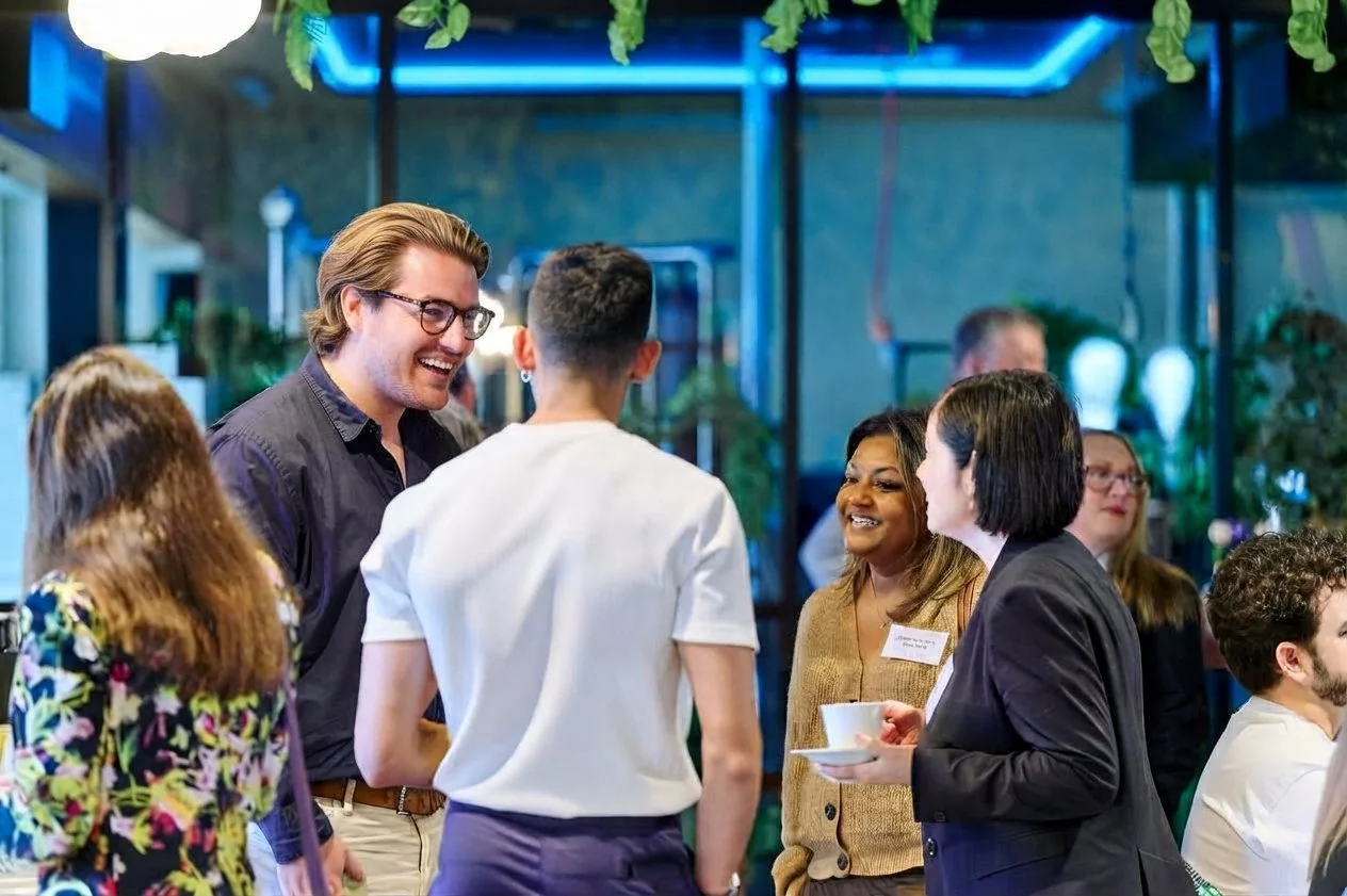 Group of diverse people engaging in conversation at a social event, indoor setting with blue neon lights and plants.